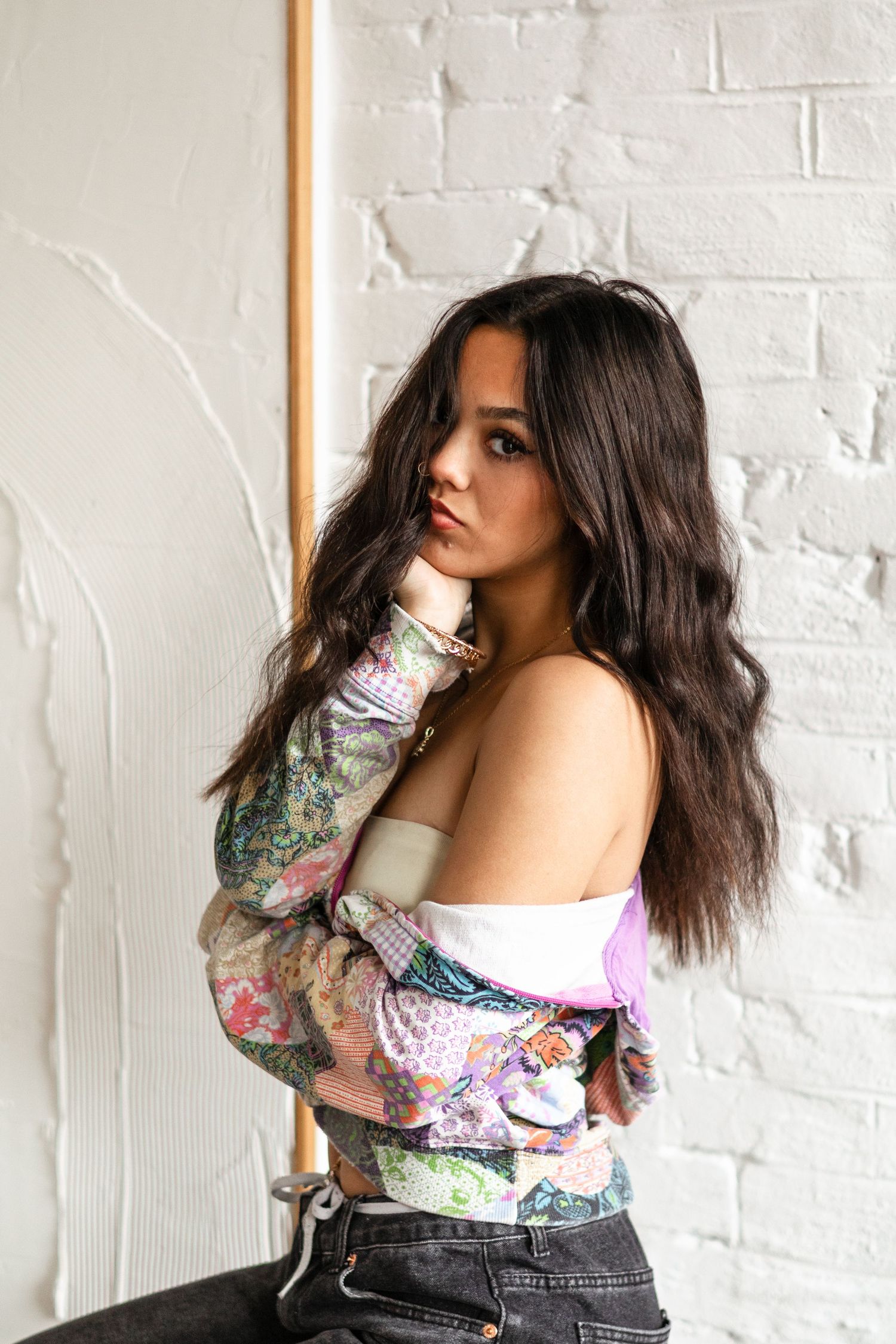 Fashionable model in colorful patterned top poses against white brick wall.