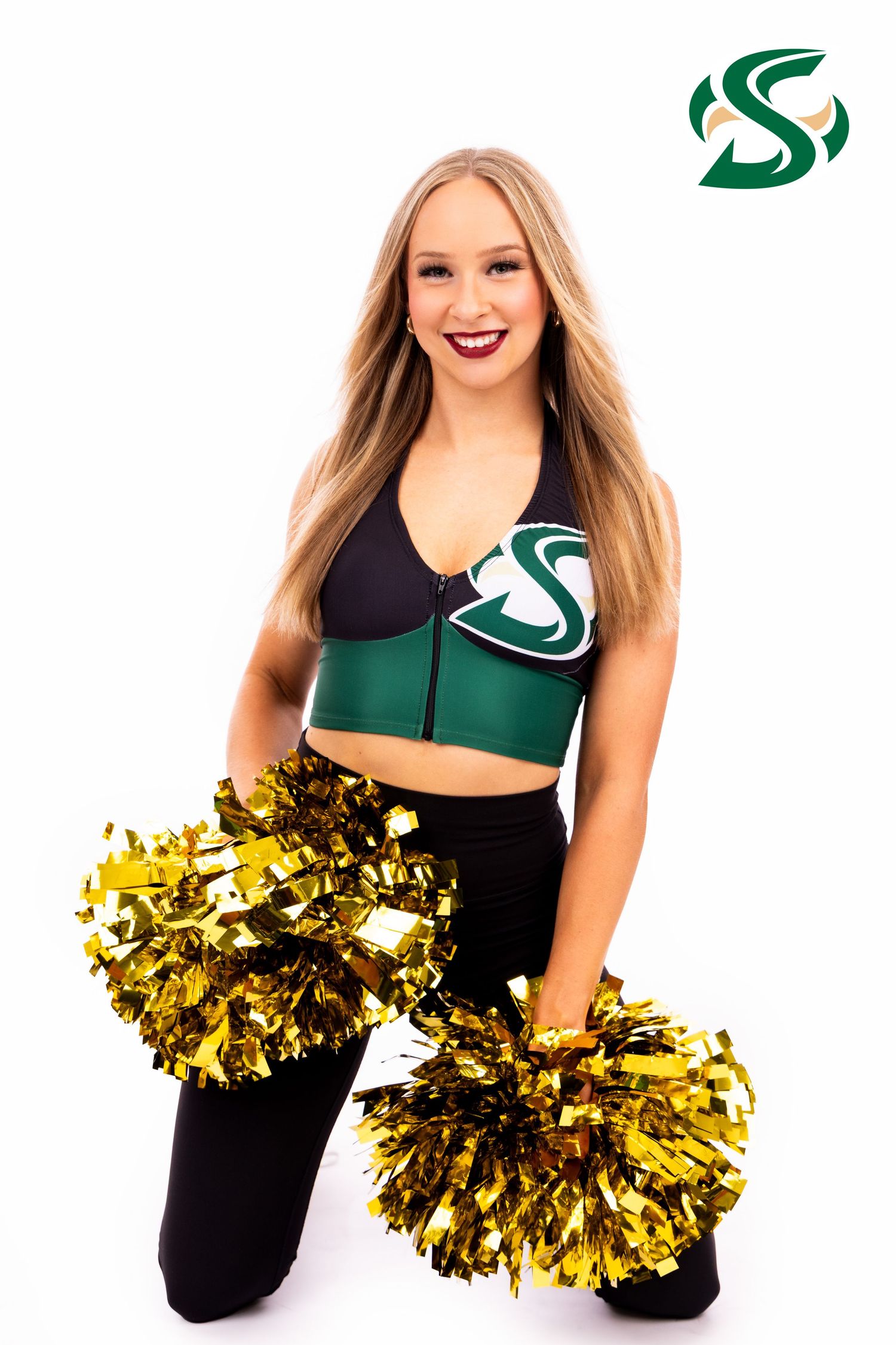 Cheerleader in dark and green uniform sits with gold pom poms in performance pose.