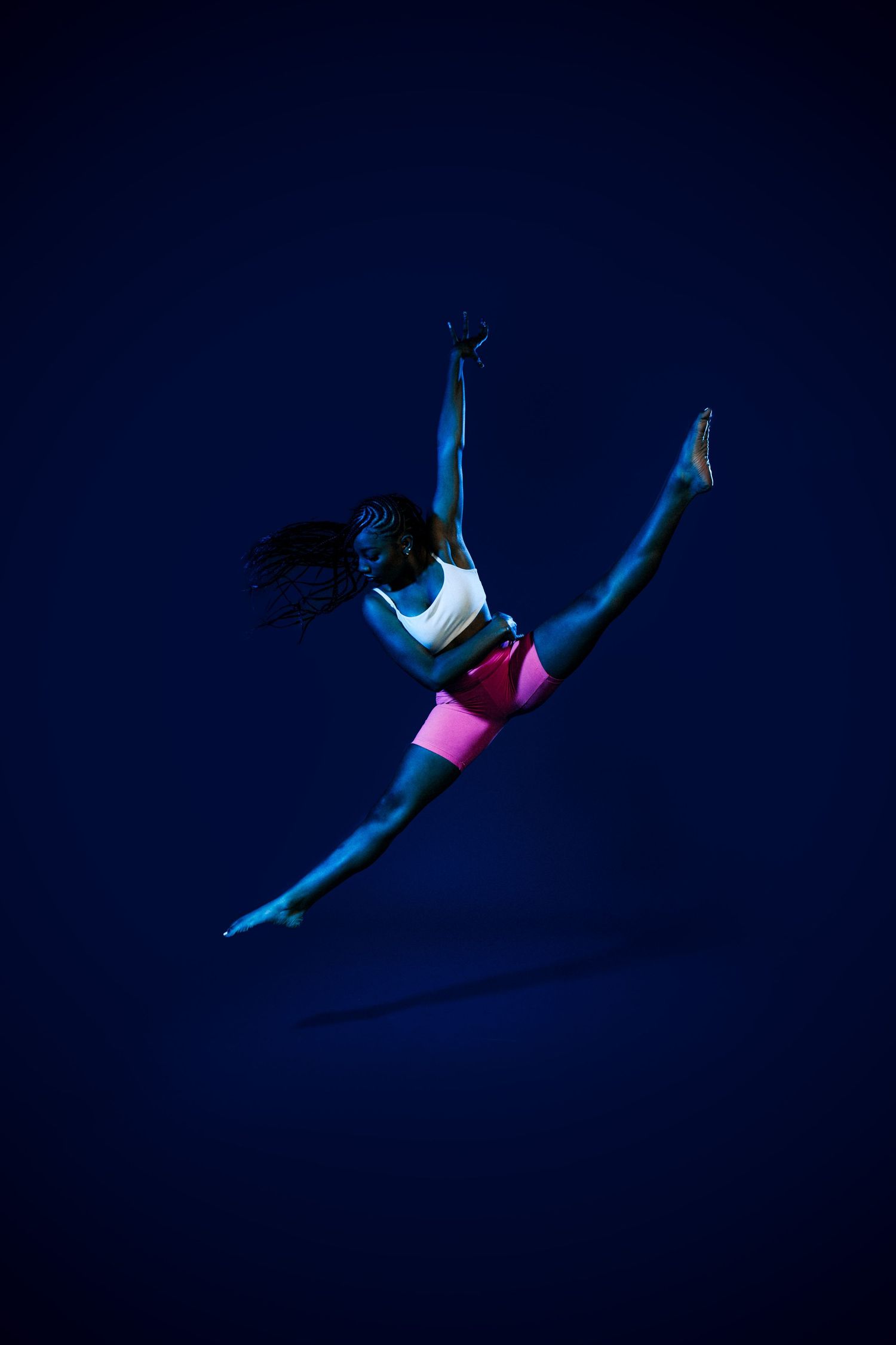 Athletic dancer performing split leap in mid-air against deep blue backdrop.
