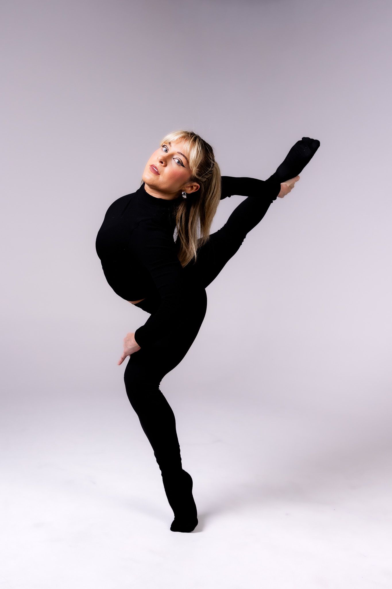 A dancer in black attire performs an elegant and expressive contemporary dance sequence against a light colored background.