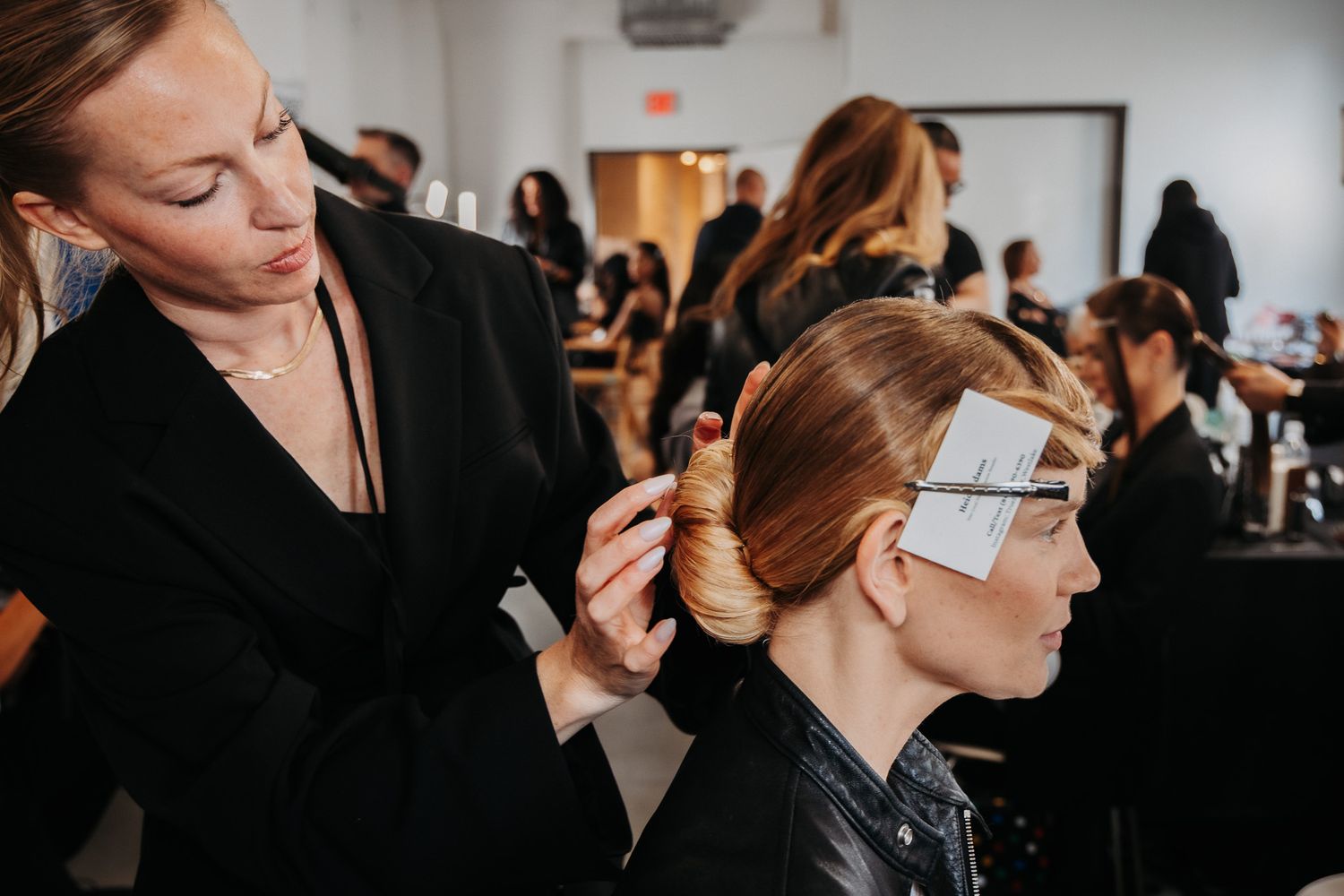 Models getting their hair and makeup done backstage at a fashion show in a white studio space.