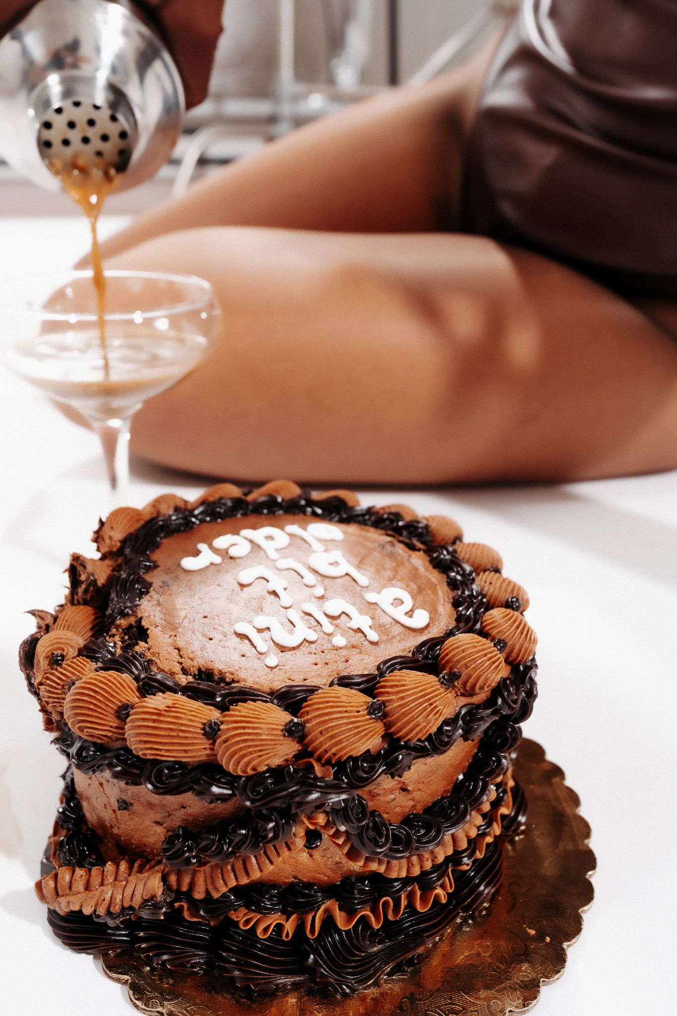 Chocolate birthday cake with decorative piping and a glass of champagne being poured in the background.