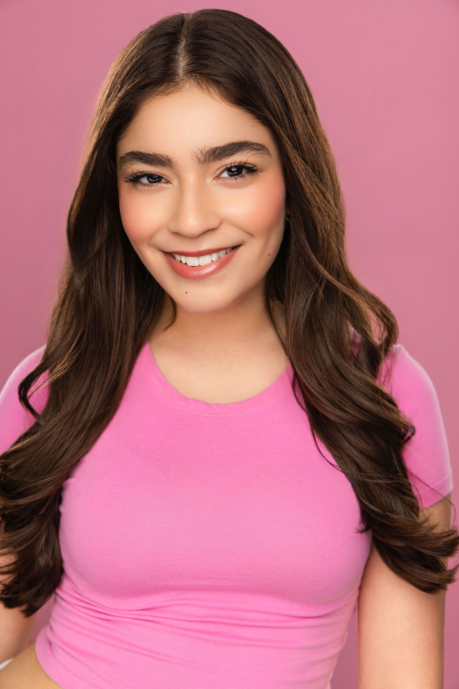 Professional headshot against pink background wearing bright pink top with flowing dark hair.