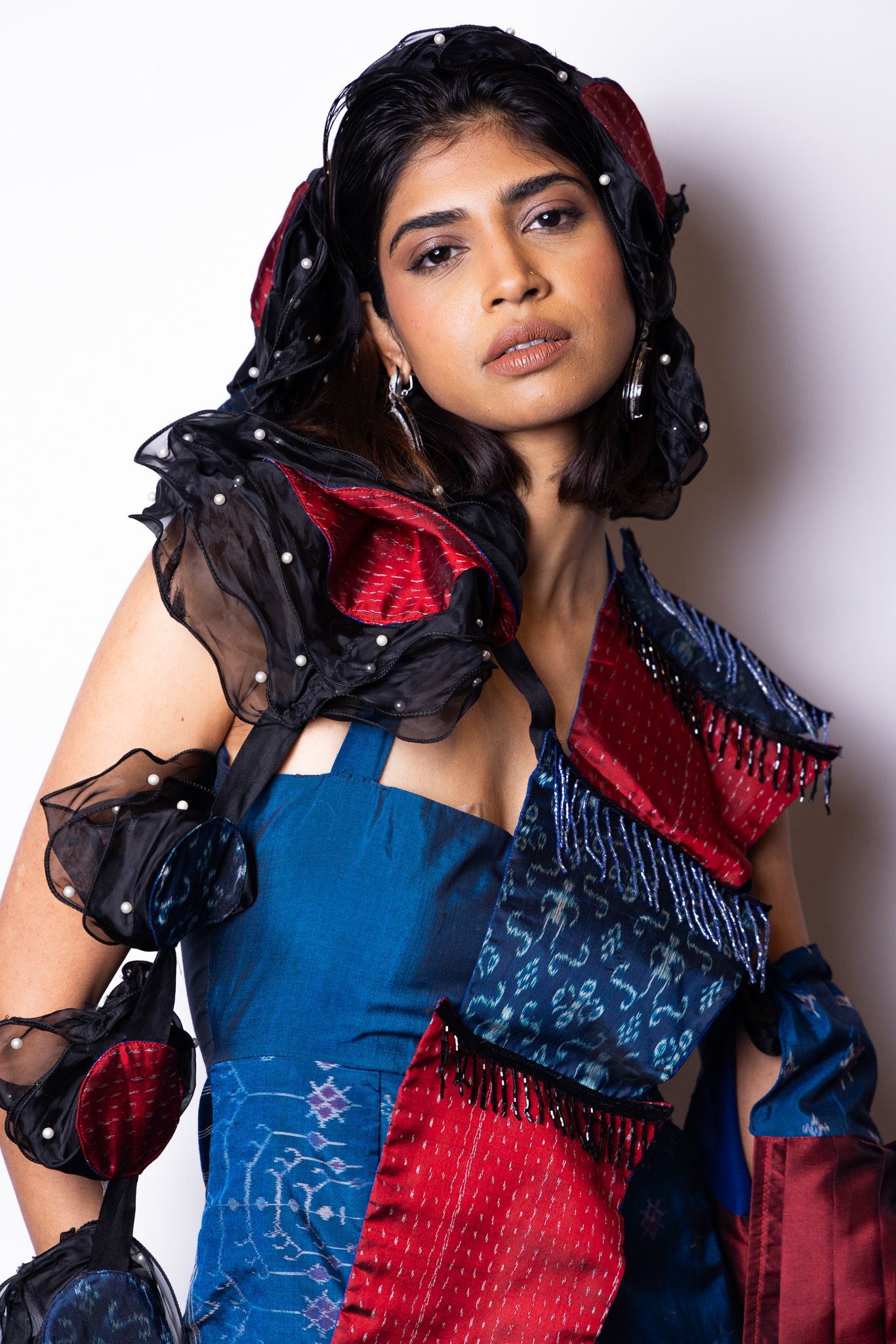 Fashion portrait in blue and red textured garment with dramatic black sheer details.