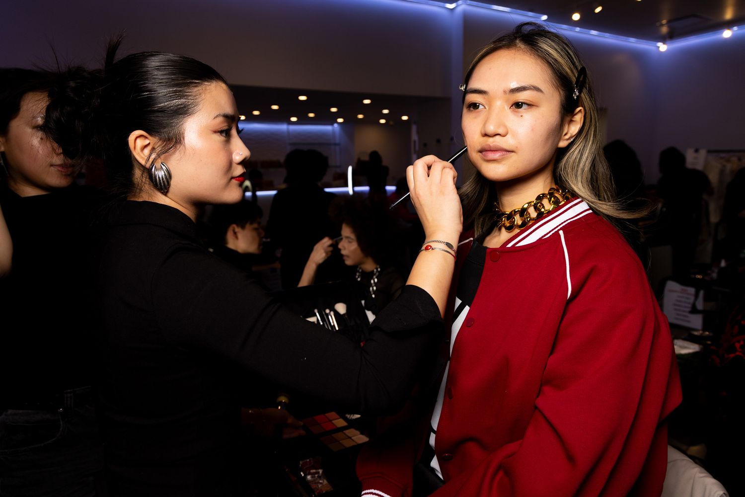 Models wearing red outfits walk the runway at a fashion show with dramatic blue lighting.