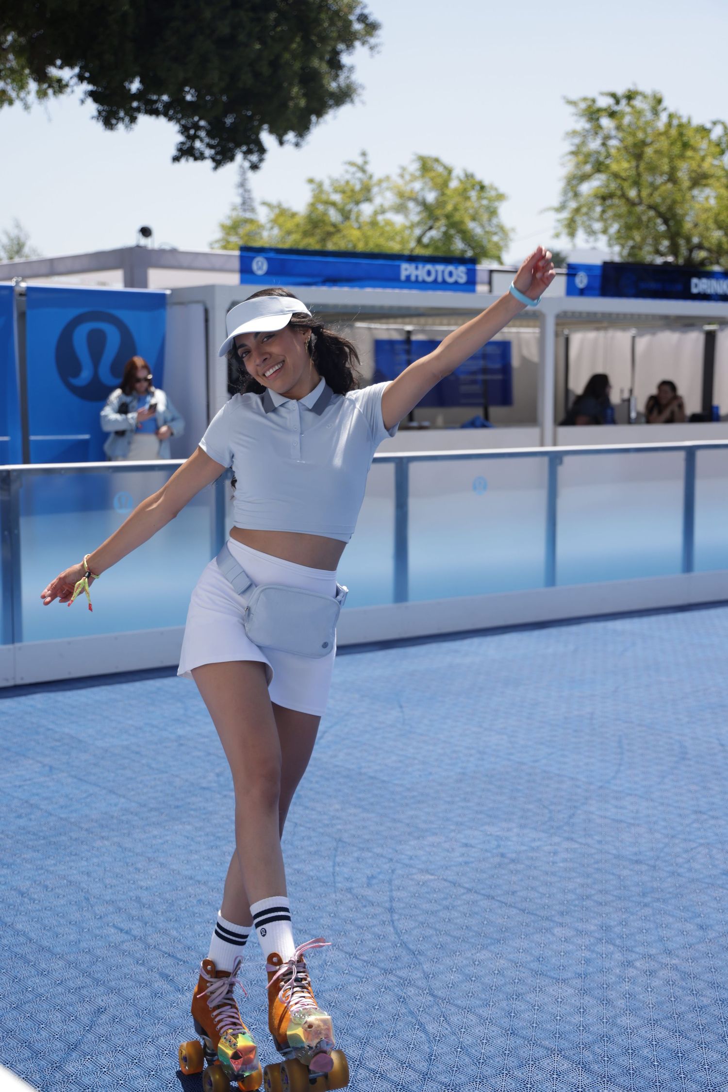 Person in white outfit and roller skates performs dance moves on a blue outdoor rink surface.