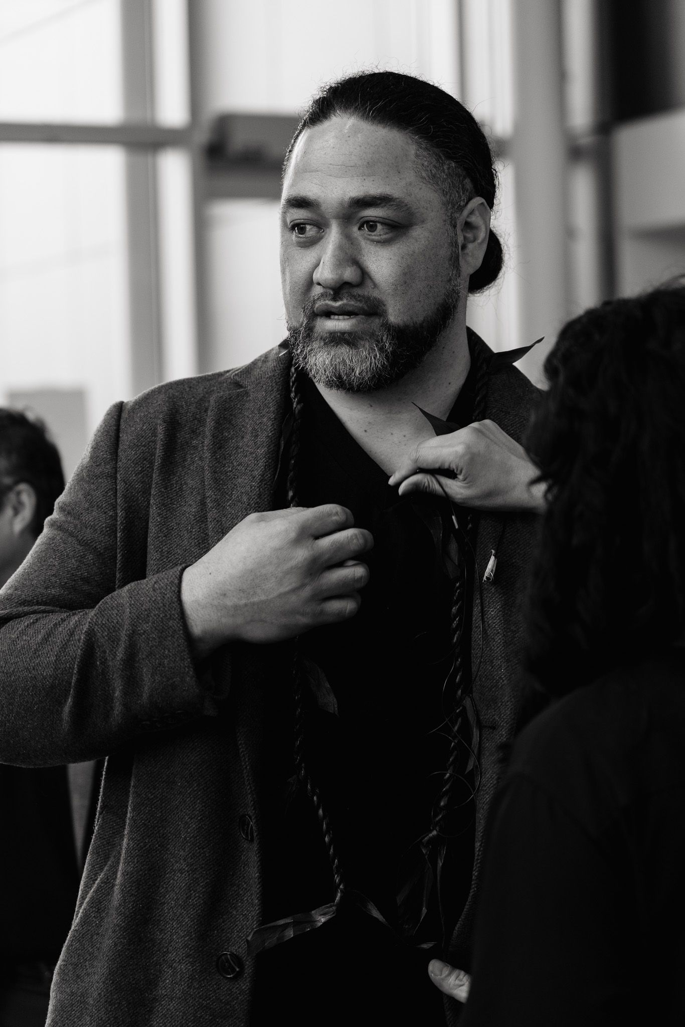 Black and white portrait of a man in a dark coat adjusting his collar against a bright window background.