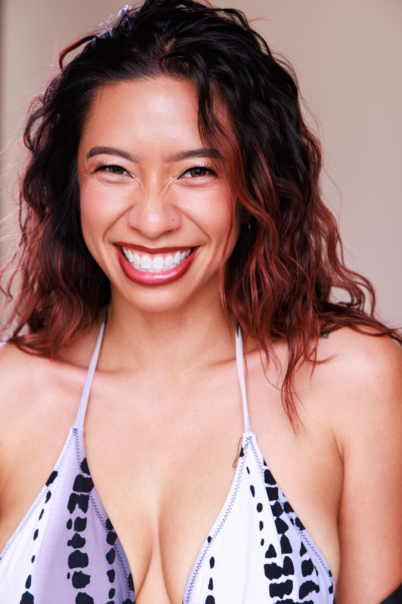 Smiling woman with curly dark hair wearing a black and white bikini top, radiating confidence and joy.