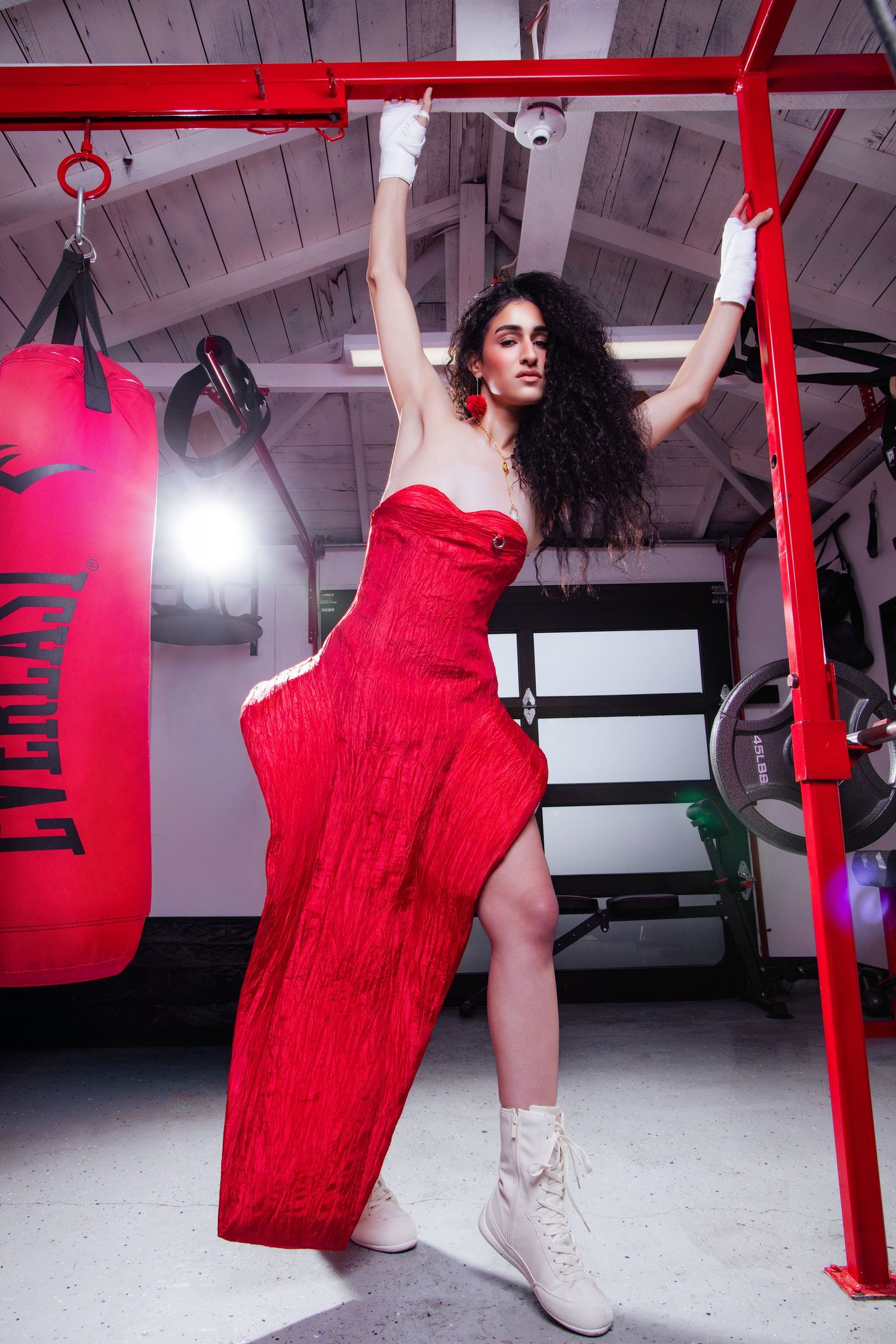 Woman in red strapless gown and white boxing gloves poses in a gym with an Everlast punching bag.