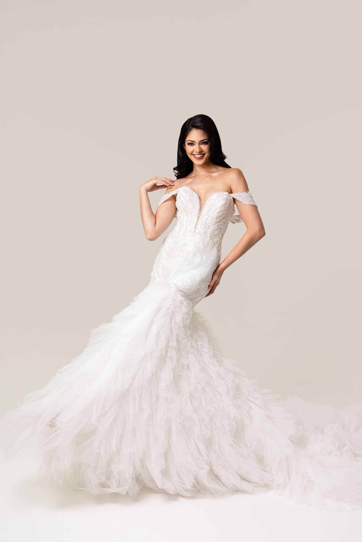 Elegant mermaid wedding gown with off-shoulder lace bodice and cascading ruffled tulle skirt on a smiling bride.