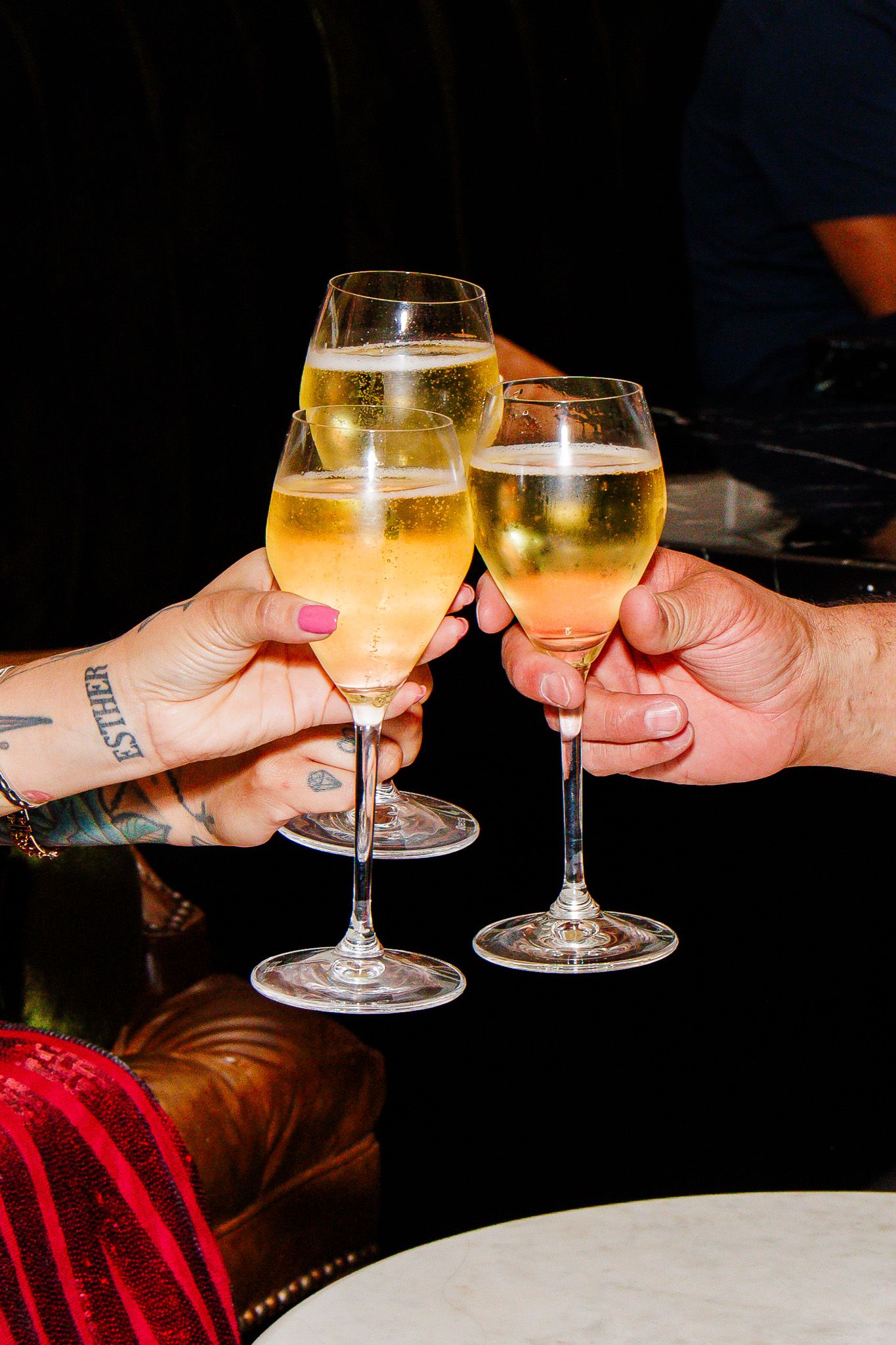 Three hands clinking champagne glasses filled with sparkling wine at a celebratory toast.
