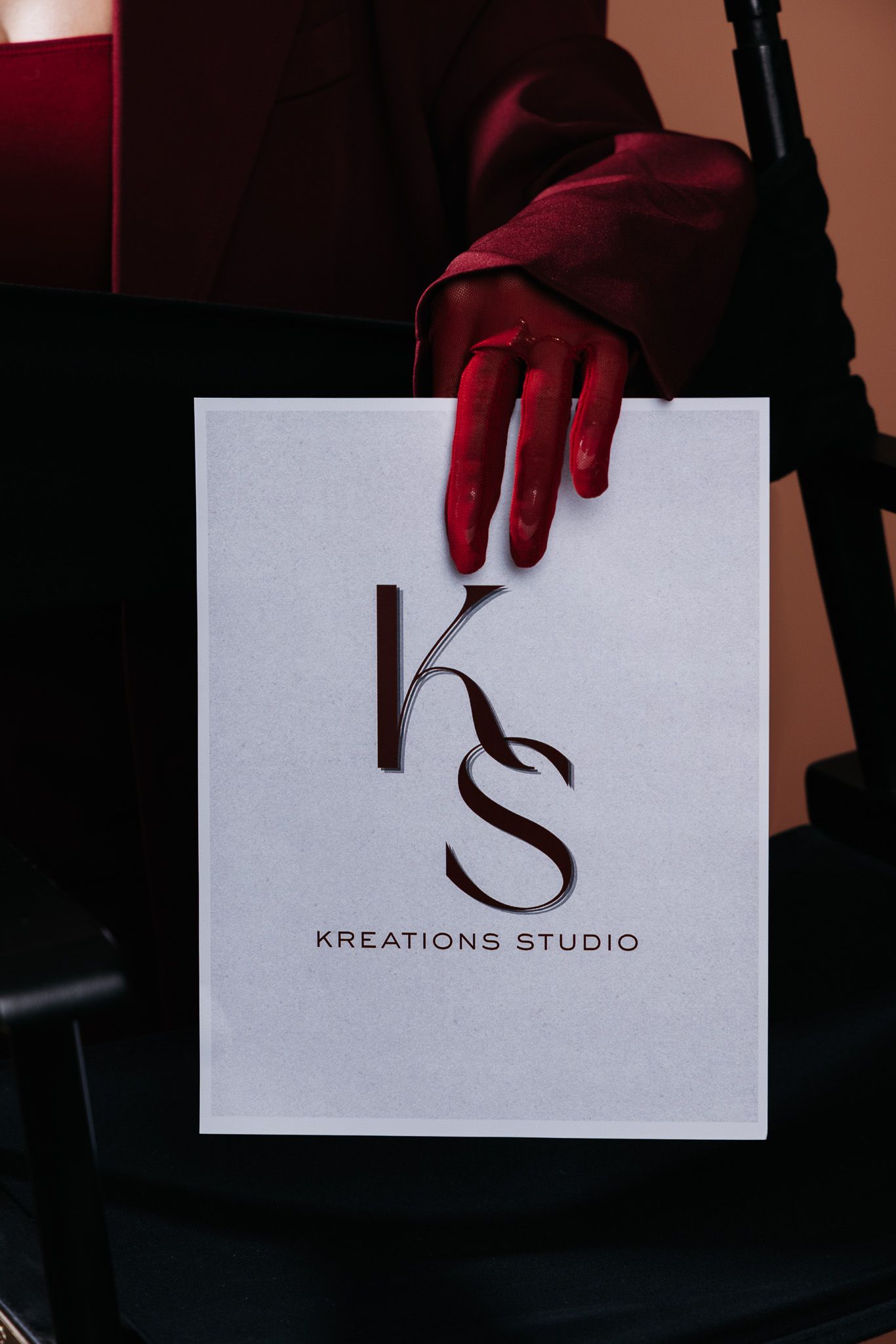 A red-gloved hand holds a white card displaying the Kreations Studio logo with elegant KS monogram lettering.