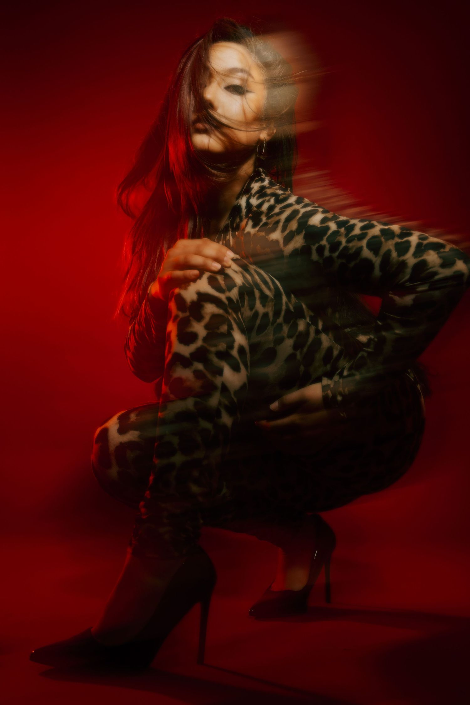 Artistic fashion portrait shot against deep red background showing leopard print dress in dramatic lighting and poses.