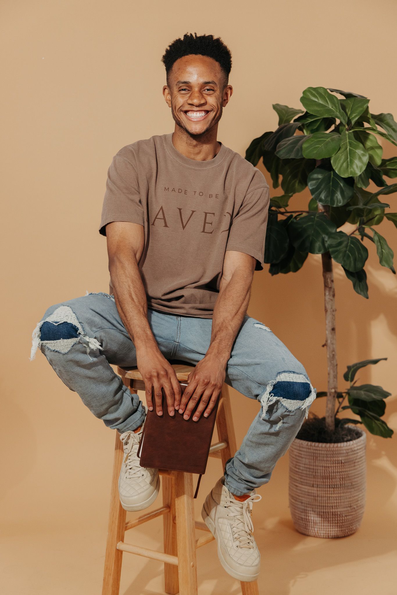Minimalist lifestyle photo shoot featuring brown t-shirt and distressed jeans against beige backdrop with houseplant.