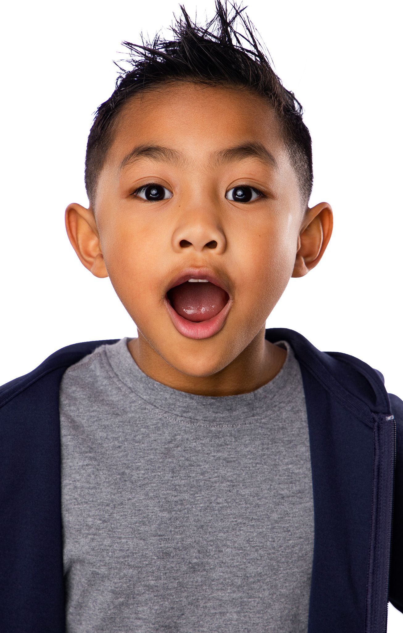 Young child with spiky hair wearing a gray t-shirt and navy jacket shows excited expression against white background.