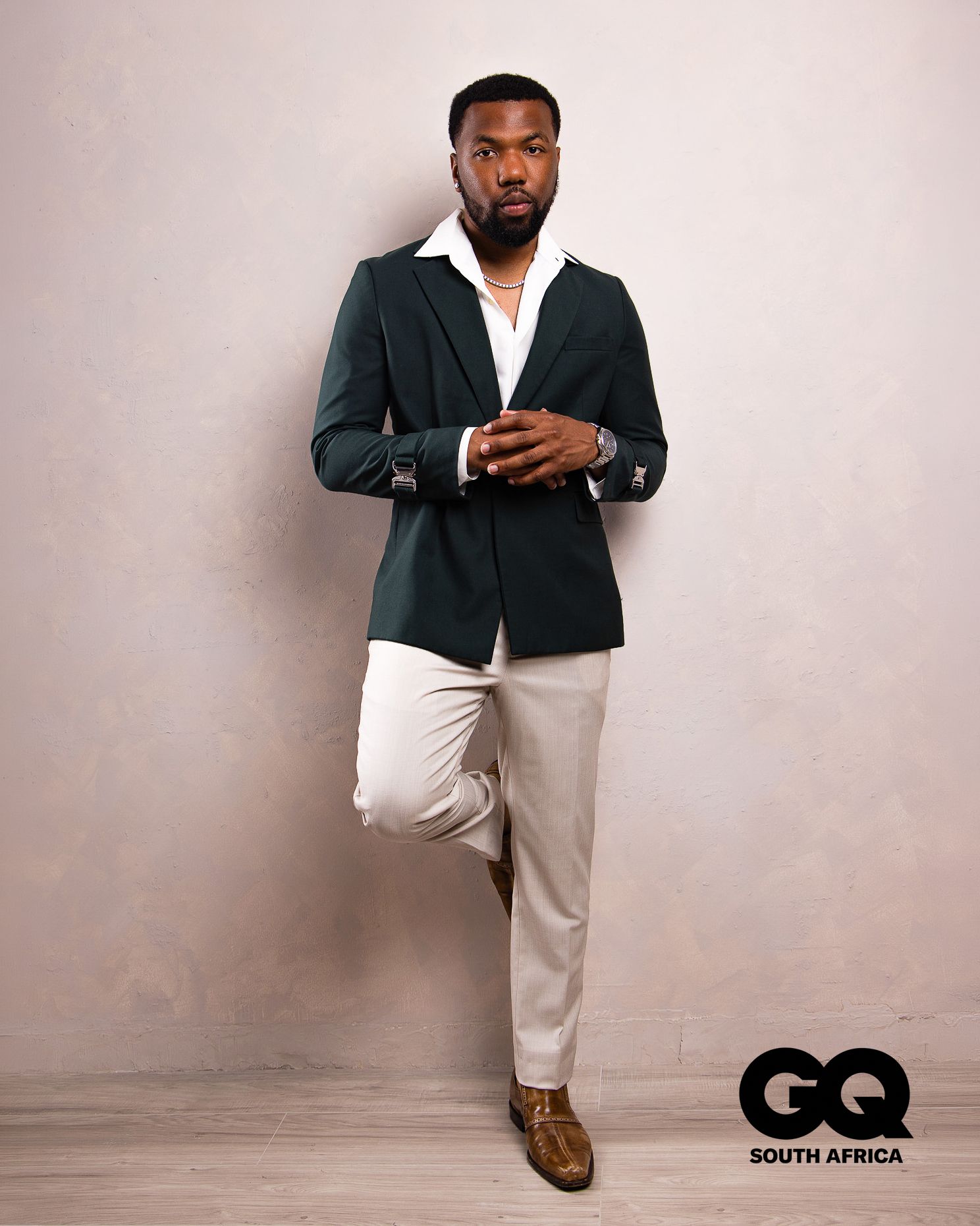 Man in dark green blazer, white shirt, and cream trousers poses confidently for GQ South Africa magazine feature.