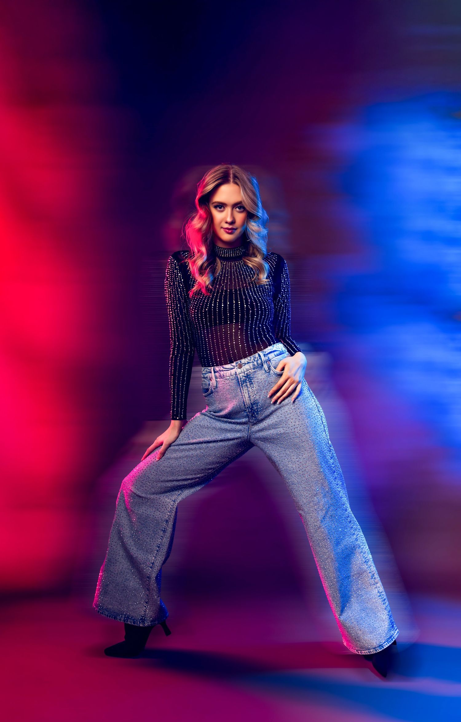 Fashion model in sparkly top and jeans poses dynamically against red and blue lighting in artistic photo series.