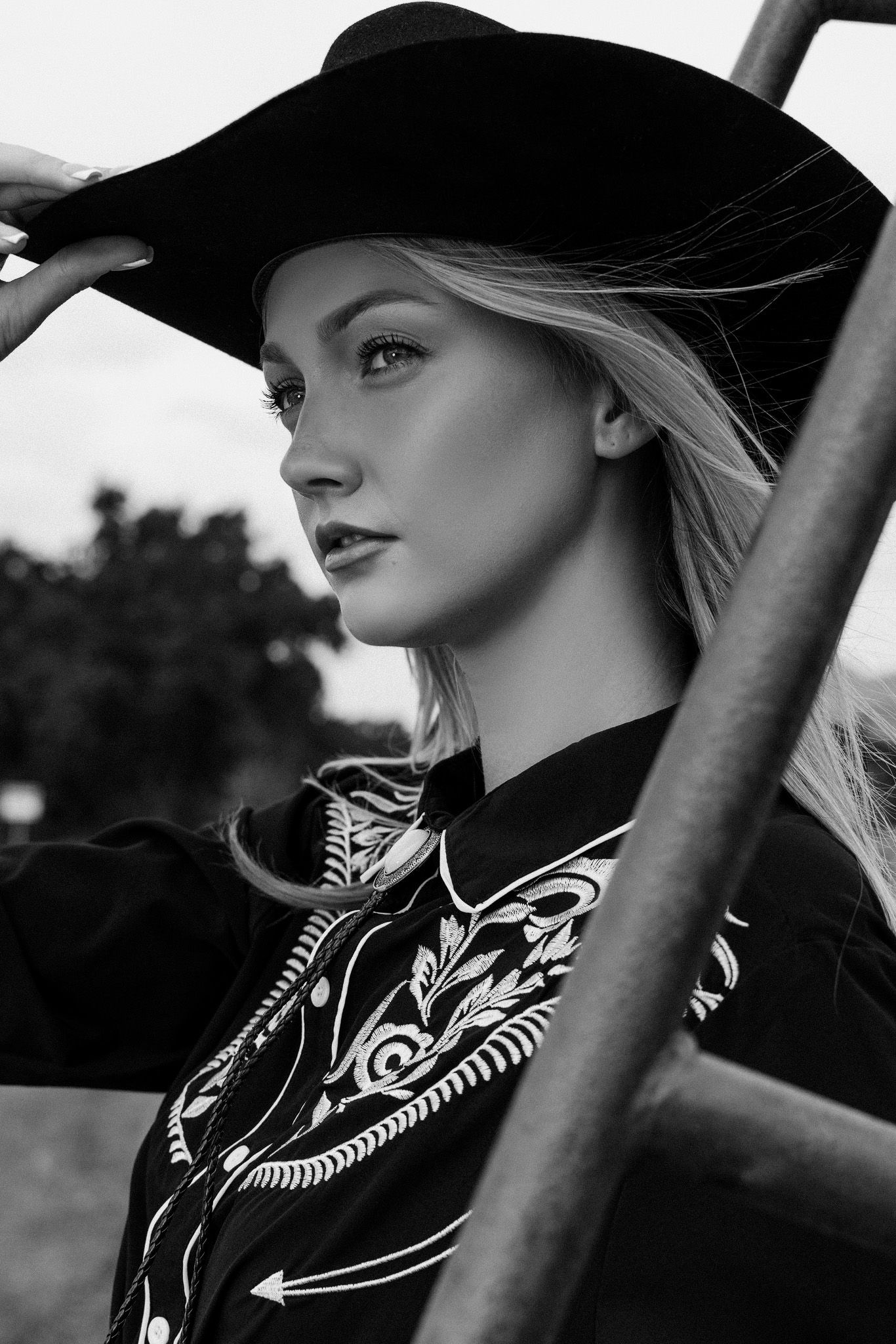 A black and white portrait of someone wearing a black hat and patterned top with flowing hair in dramatic lighting.