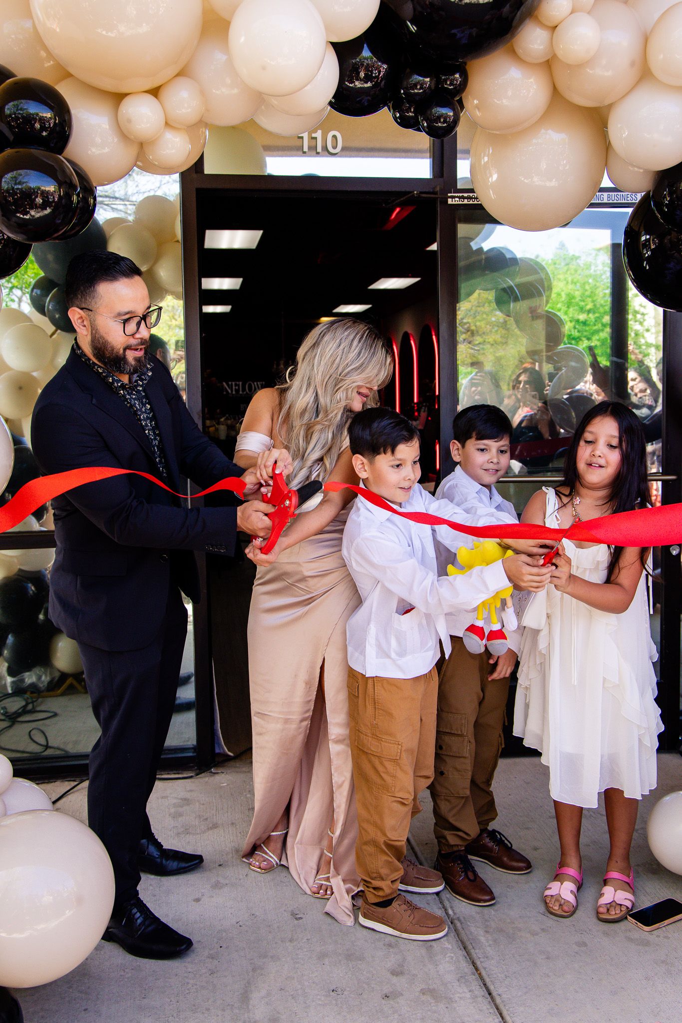 Ribbon cutting ceremony with balloons at a business opening featuring adults and children in formal attire.