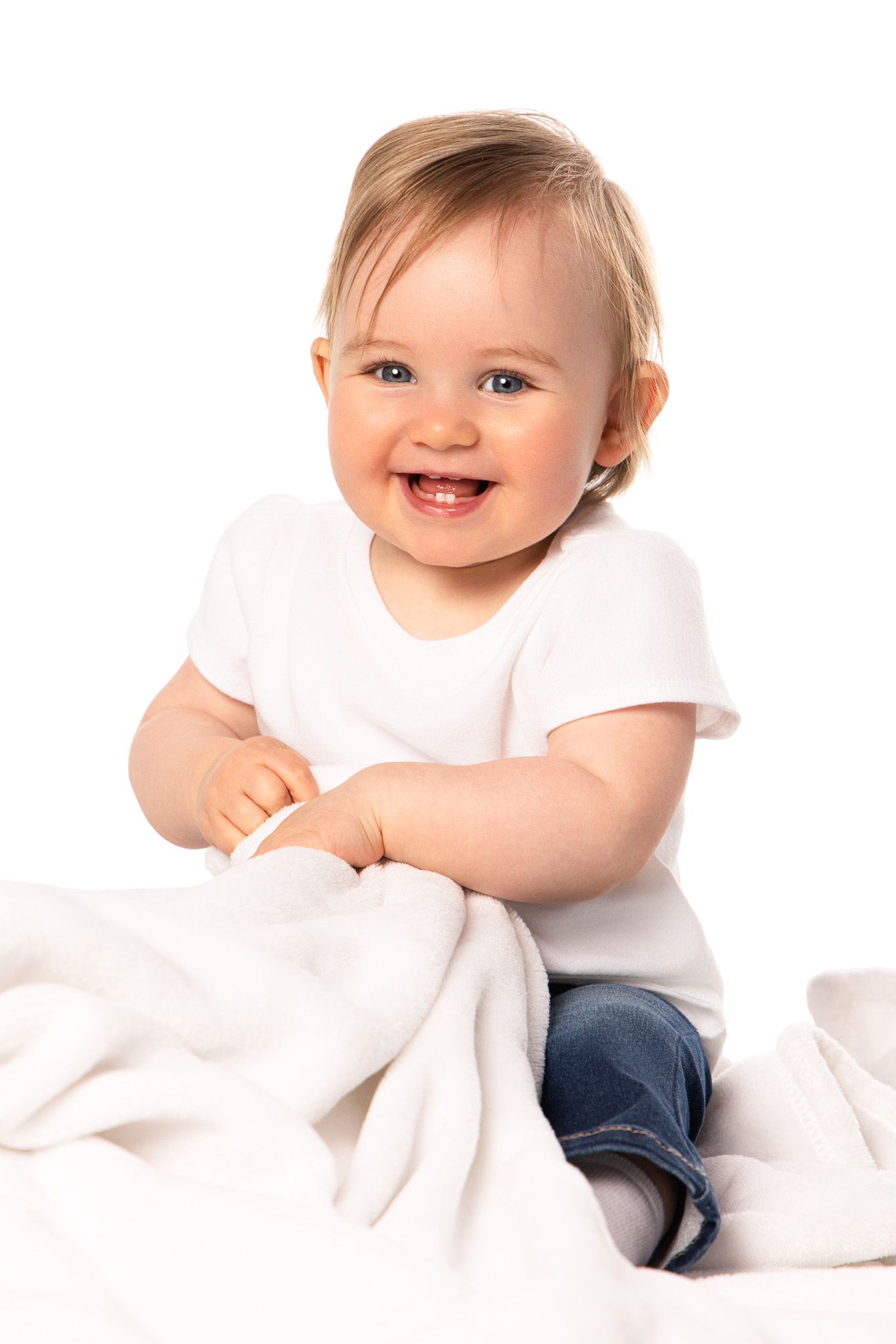 Baby wearing white shirt and jeans lying on white background showing playful expressions.