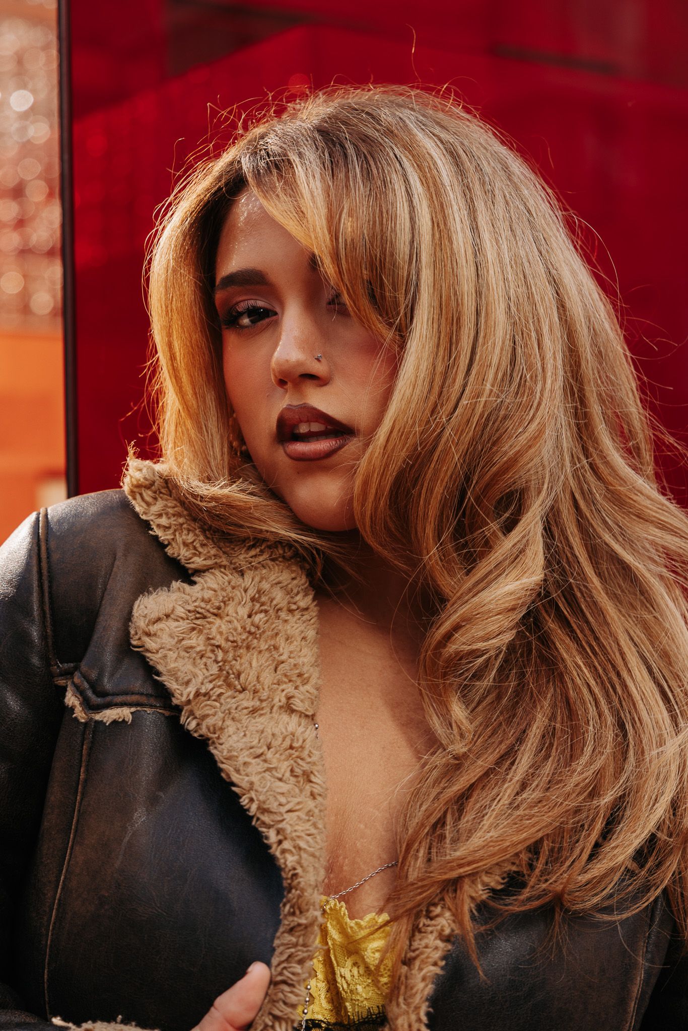 Fashion portrait with wavy blonde hair, red lipstick, and fur collar against a warm-toned background.