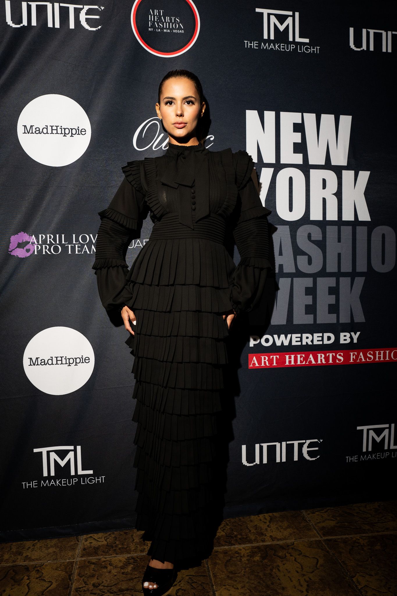 Model showcases black ruffled dress against New York Fashion Week backdrop at industry event.