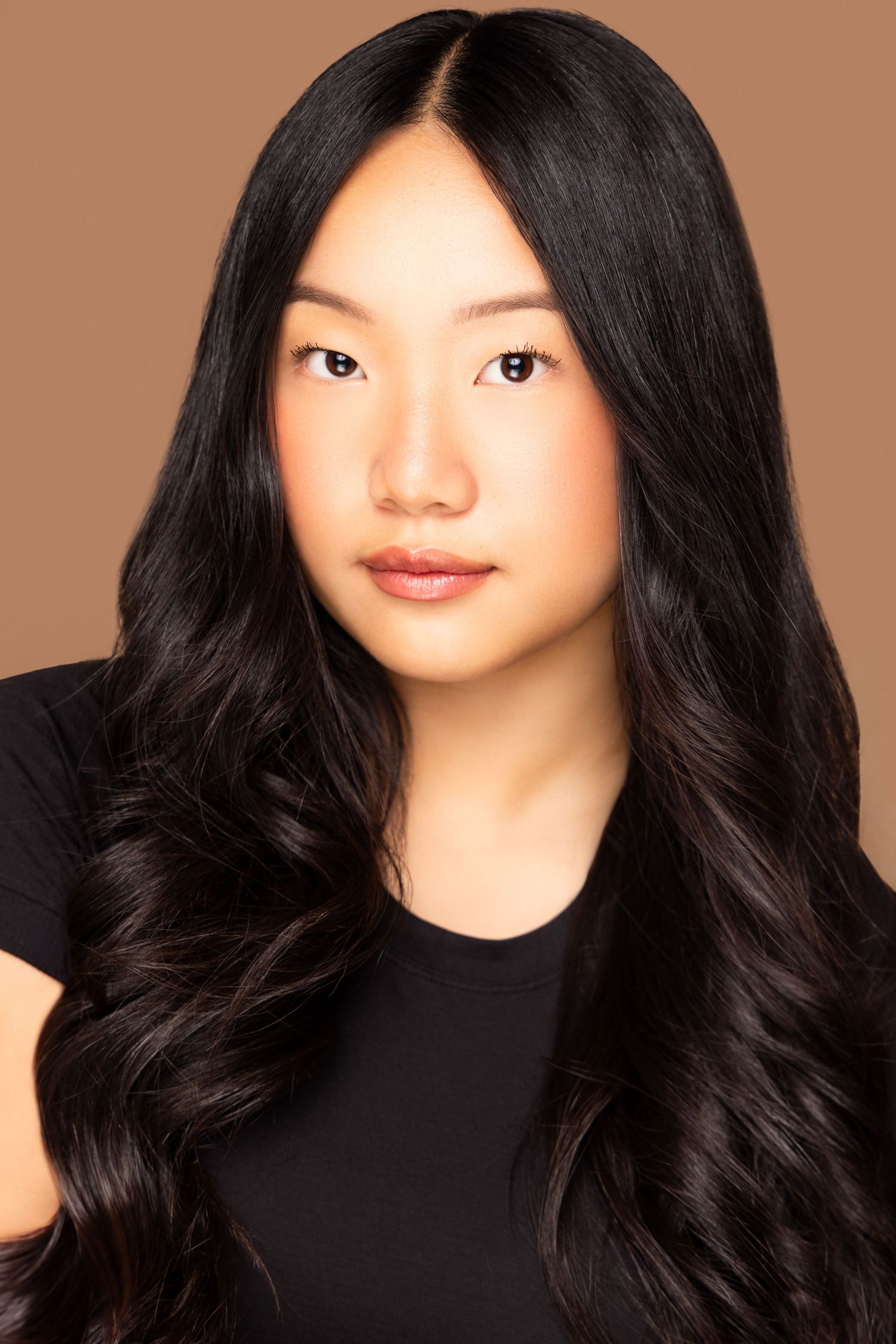 Studio beauty portrait with flowing dark hair against warm brown background.