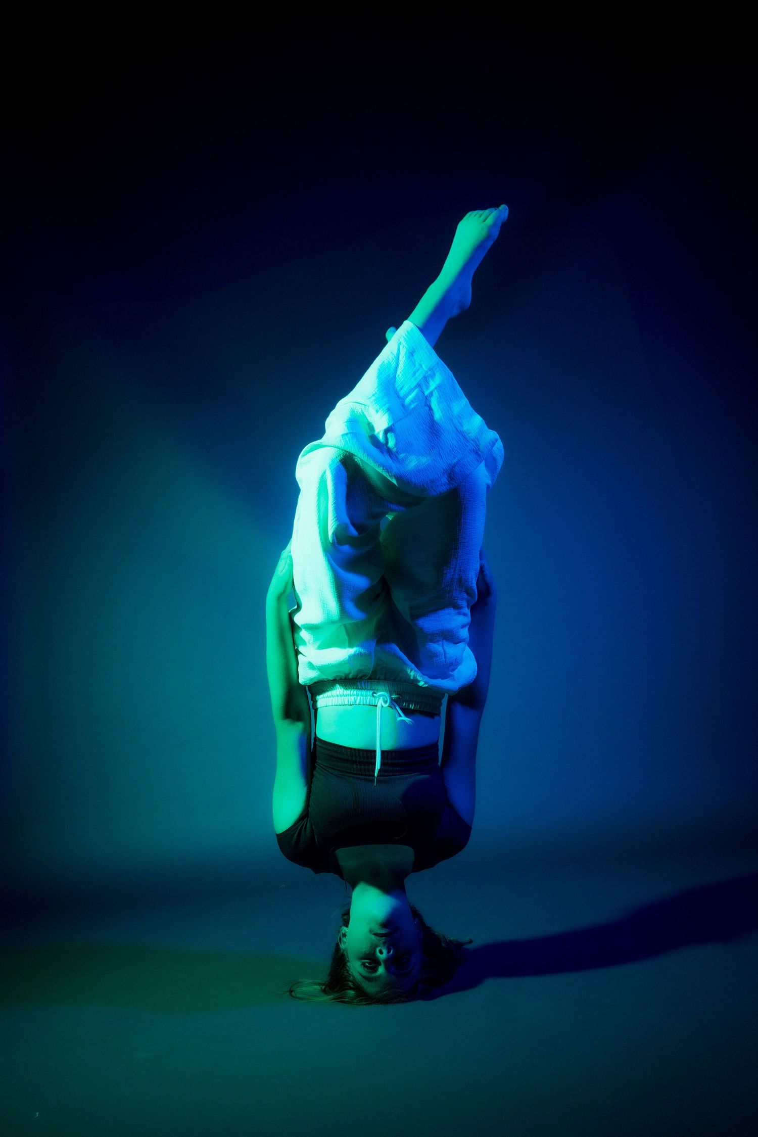 Abstract dance pose captured in ethereal blue-green lighting creating mysterious silhouette effect.