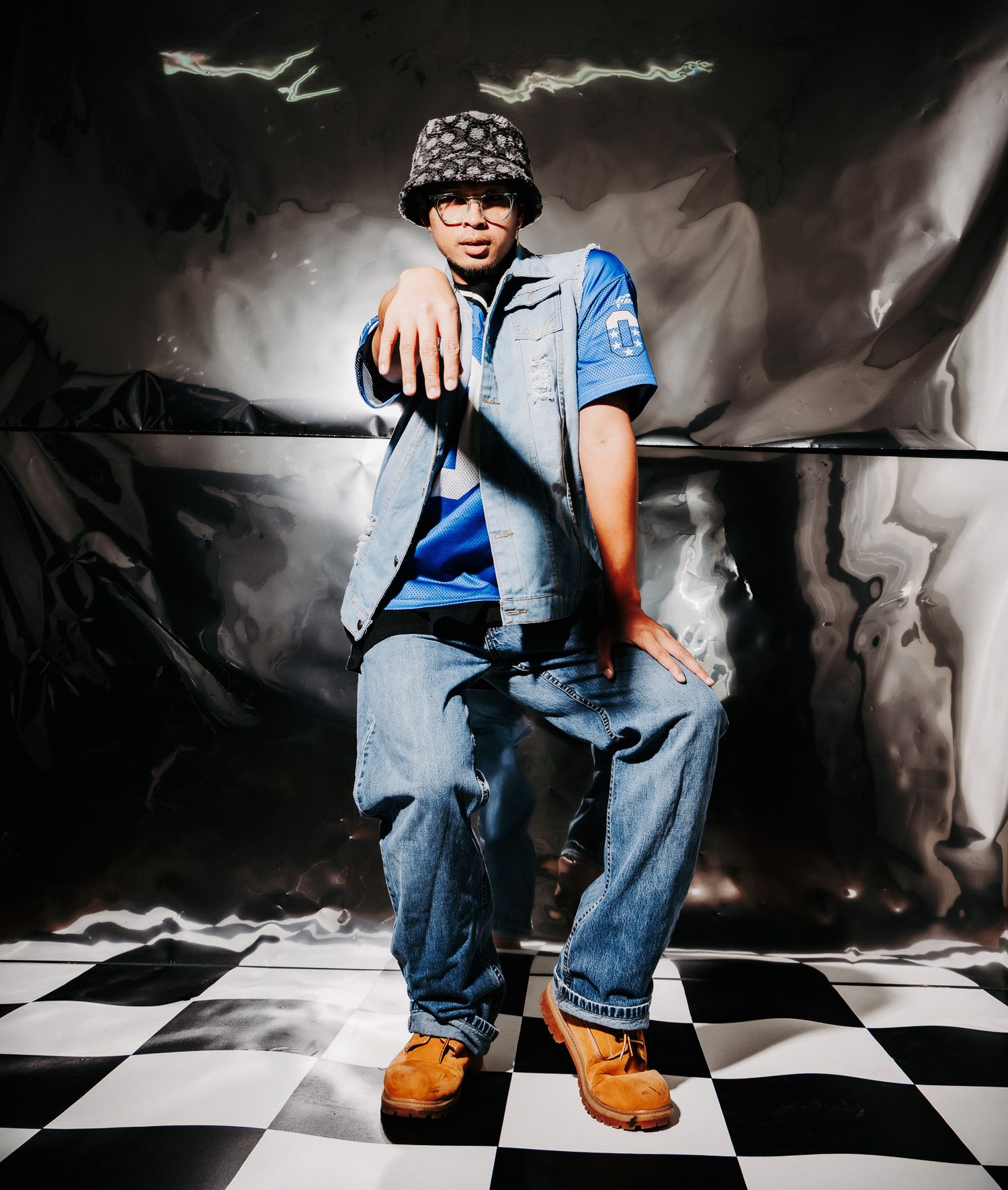 Person in blue shirt and jeans sits on checkered floor with dramatic lighting and artistic shadows.