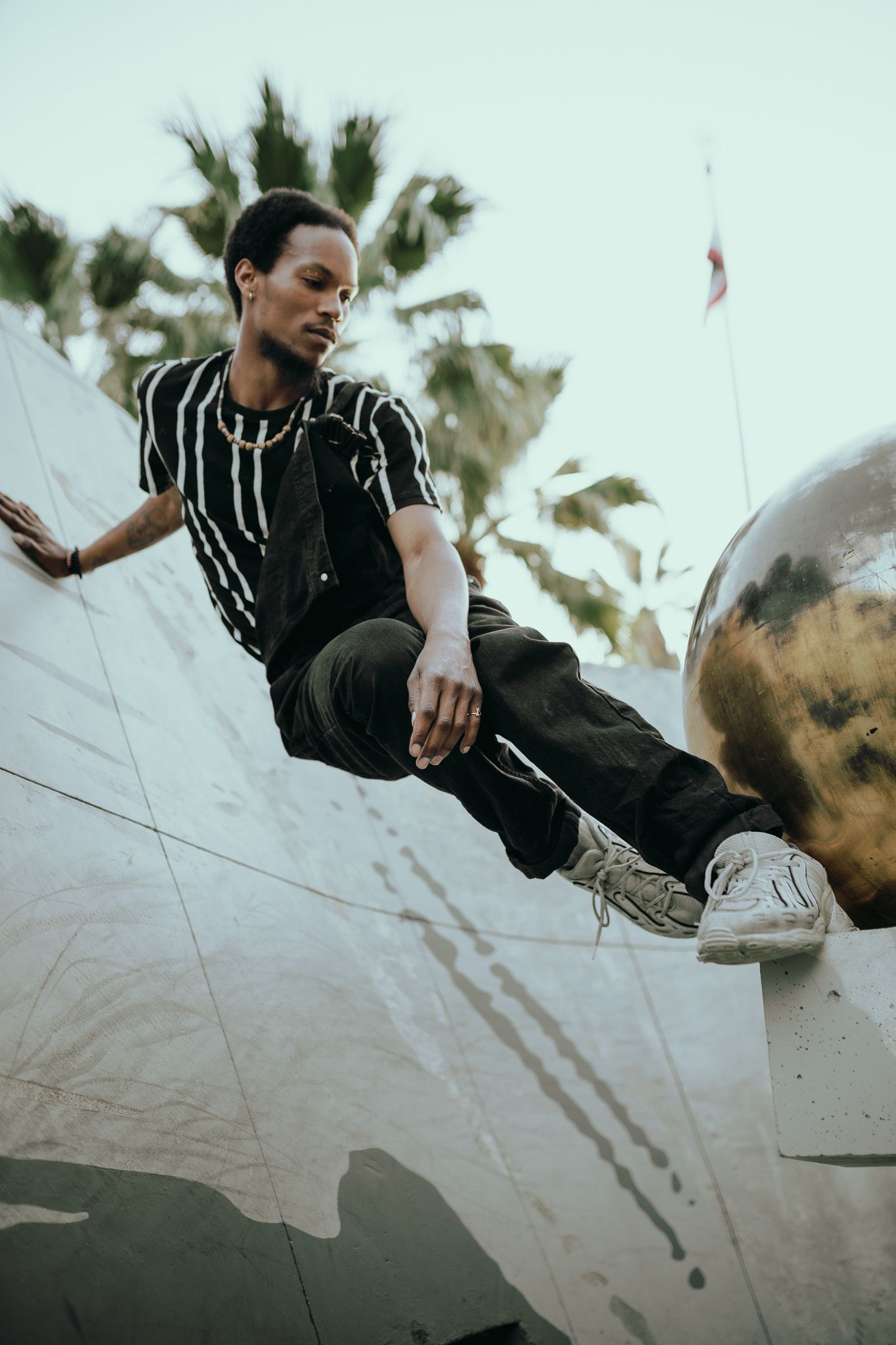 A person wearing a black outfit performs dynamic movements outdoors with palm trees in the background.
