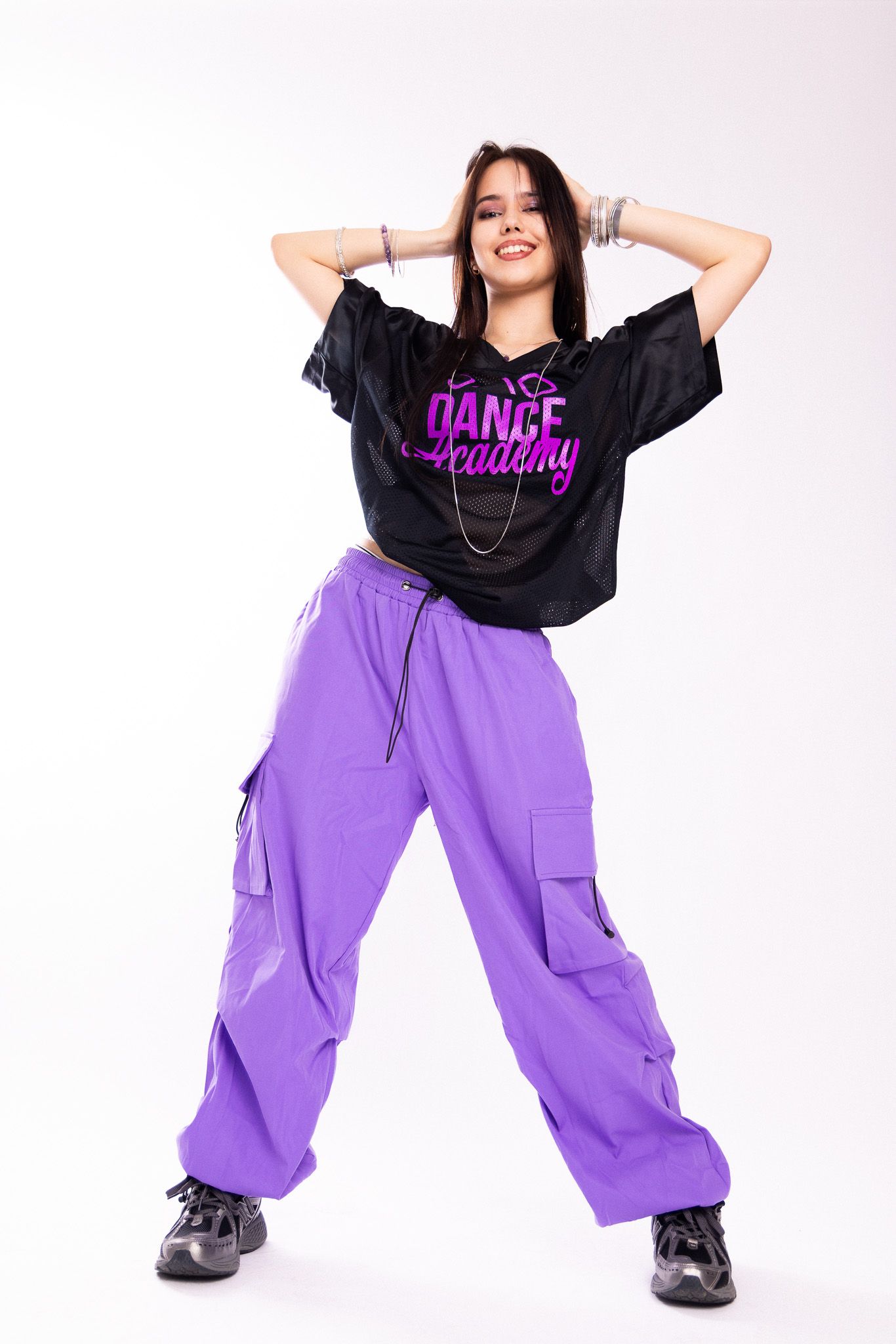 Person in streetwear outfit strikes dynamic dance poses wearing purple cargo pants and black graphic tee.