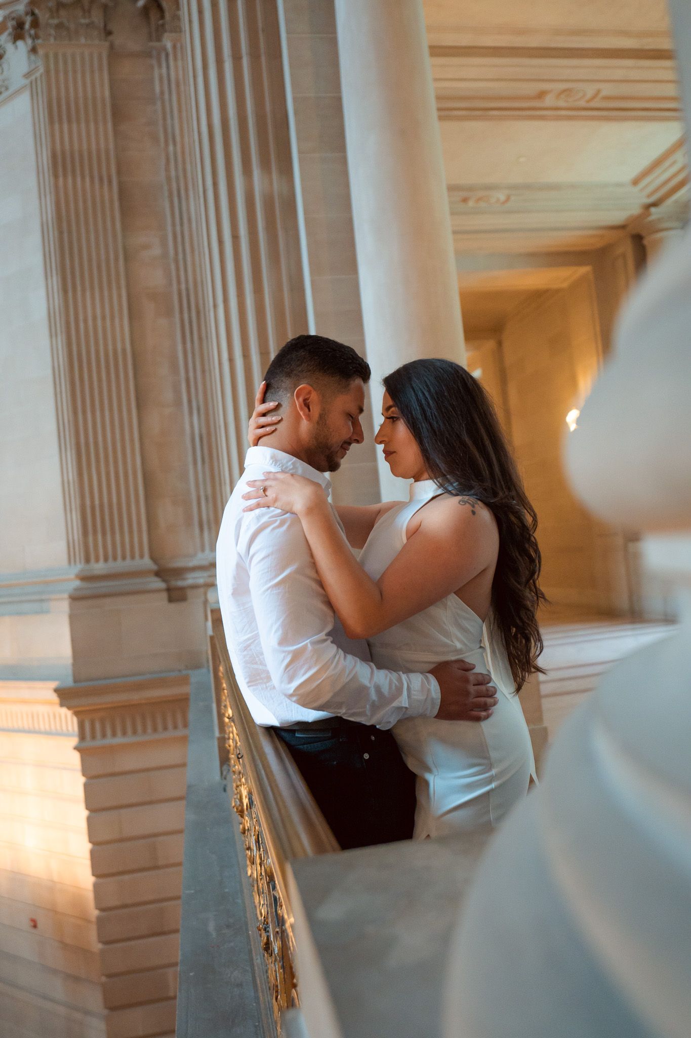 A romantic couple shares an intimate moment in an elegant hallway with classical columns and warm lighting.
