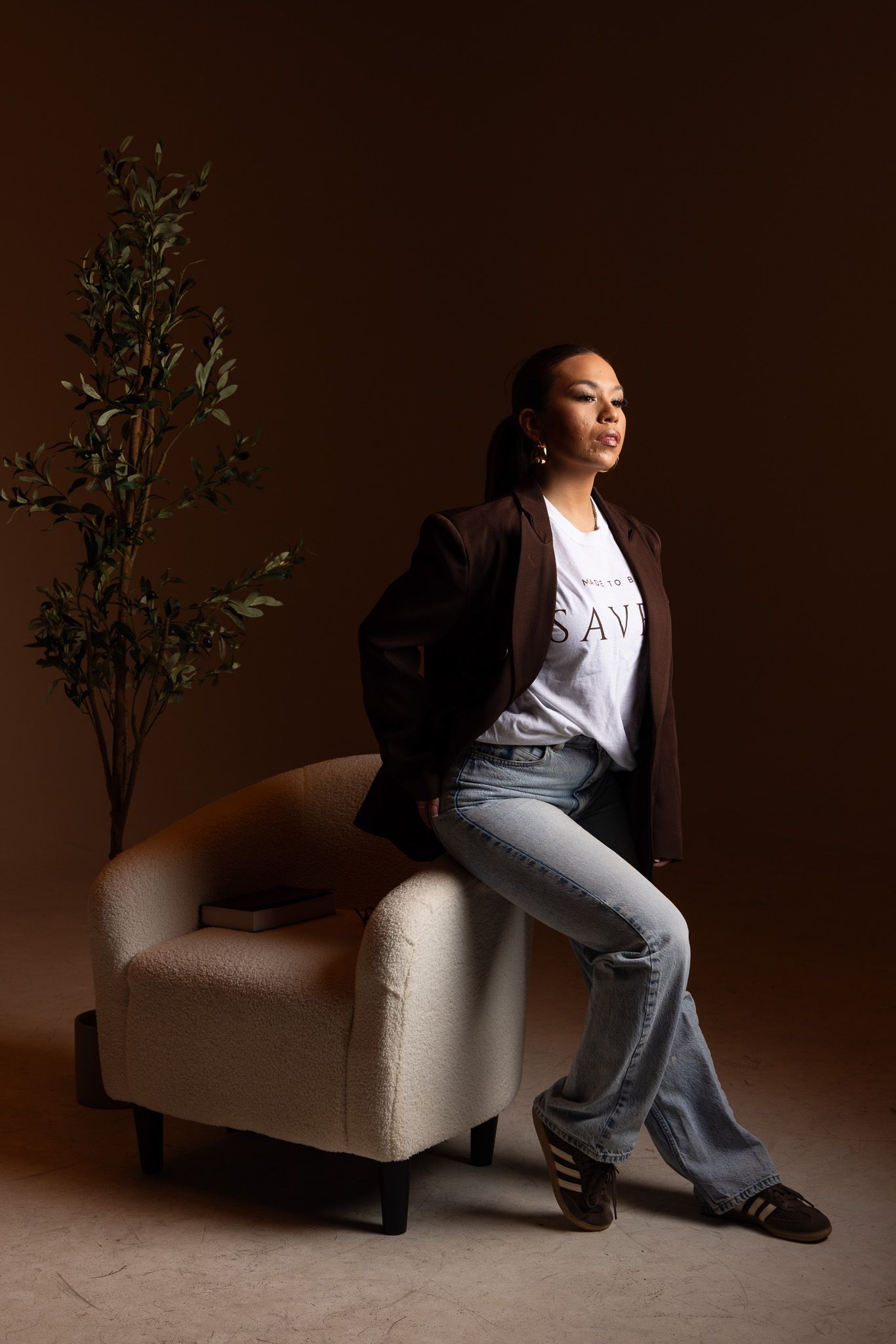 Artistic series of portraits showing figure in white top and gray pants posing on cream colored armchair against dark backdrop.