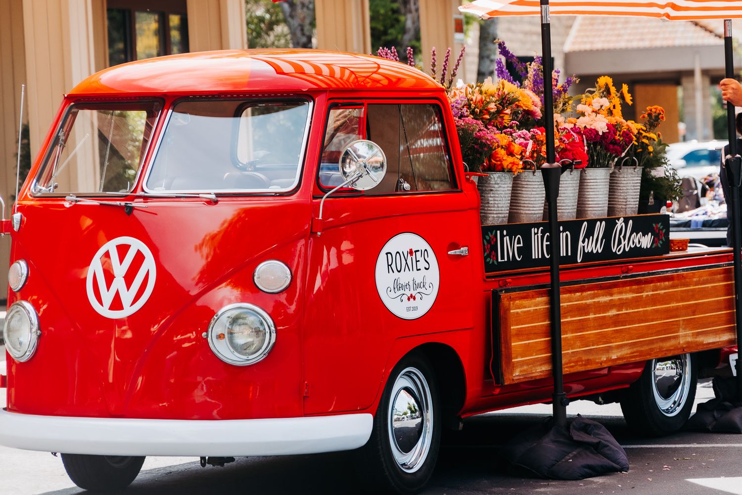 Red vintage Volkswagen bus flower truck loaded with colorful floral arrangements at outdoor event.
