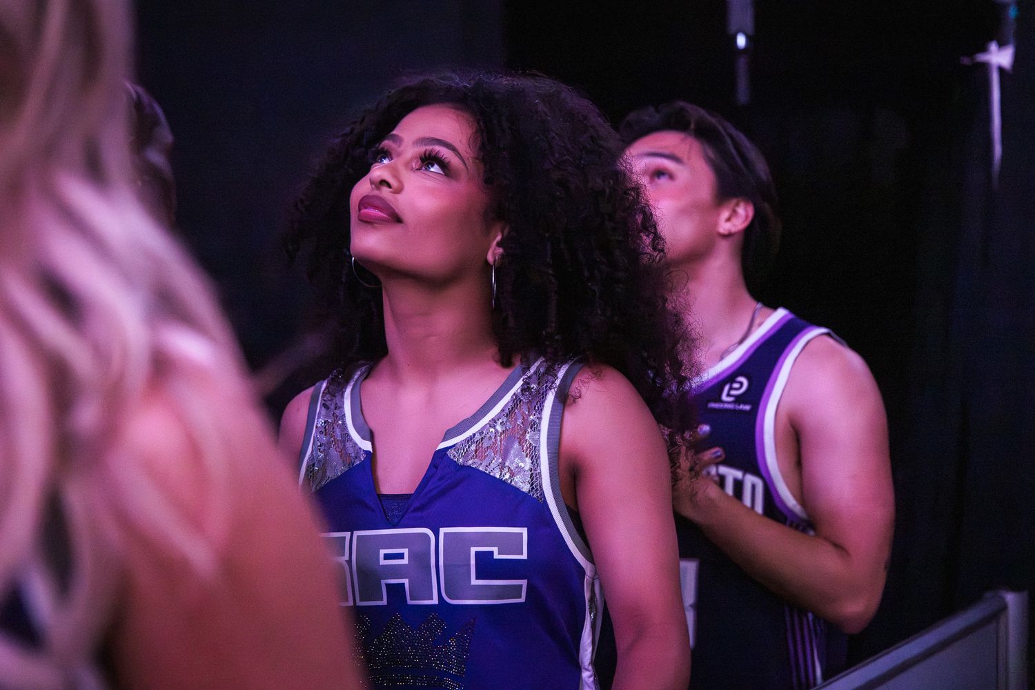 A woman in a SAC cheerleader uniform looks up backstage at a Sacramento Kings game.