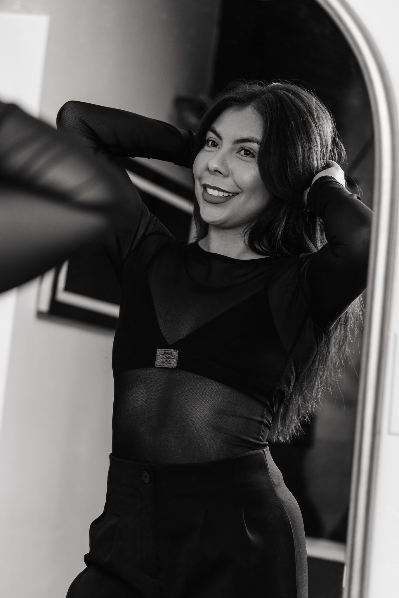 Black and white portrait of someone posing in a cropped top and skirt against an arched doorway.