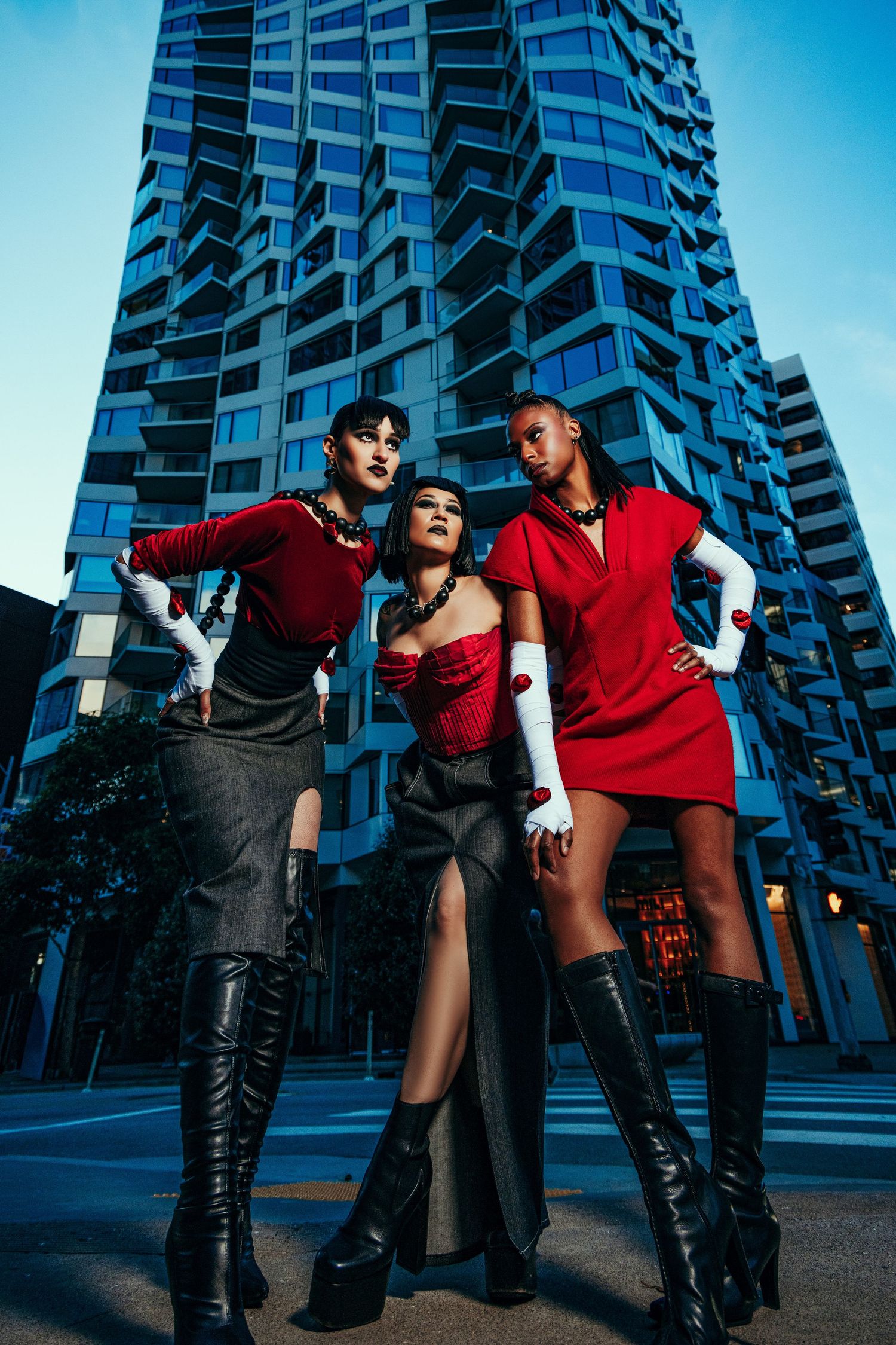 Fashion photoshoot with models in black and red outfits posing dramatically against modern glass building.