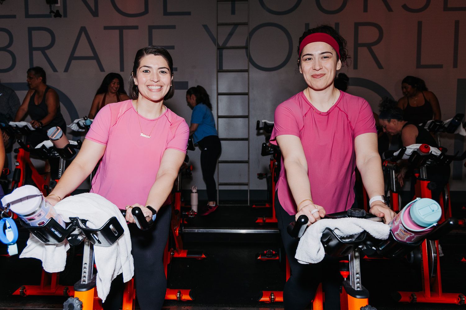 A person in a pink shirt performs an exercise routine on a stationary bike during a cycling class.