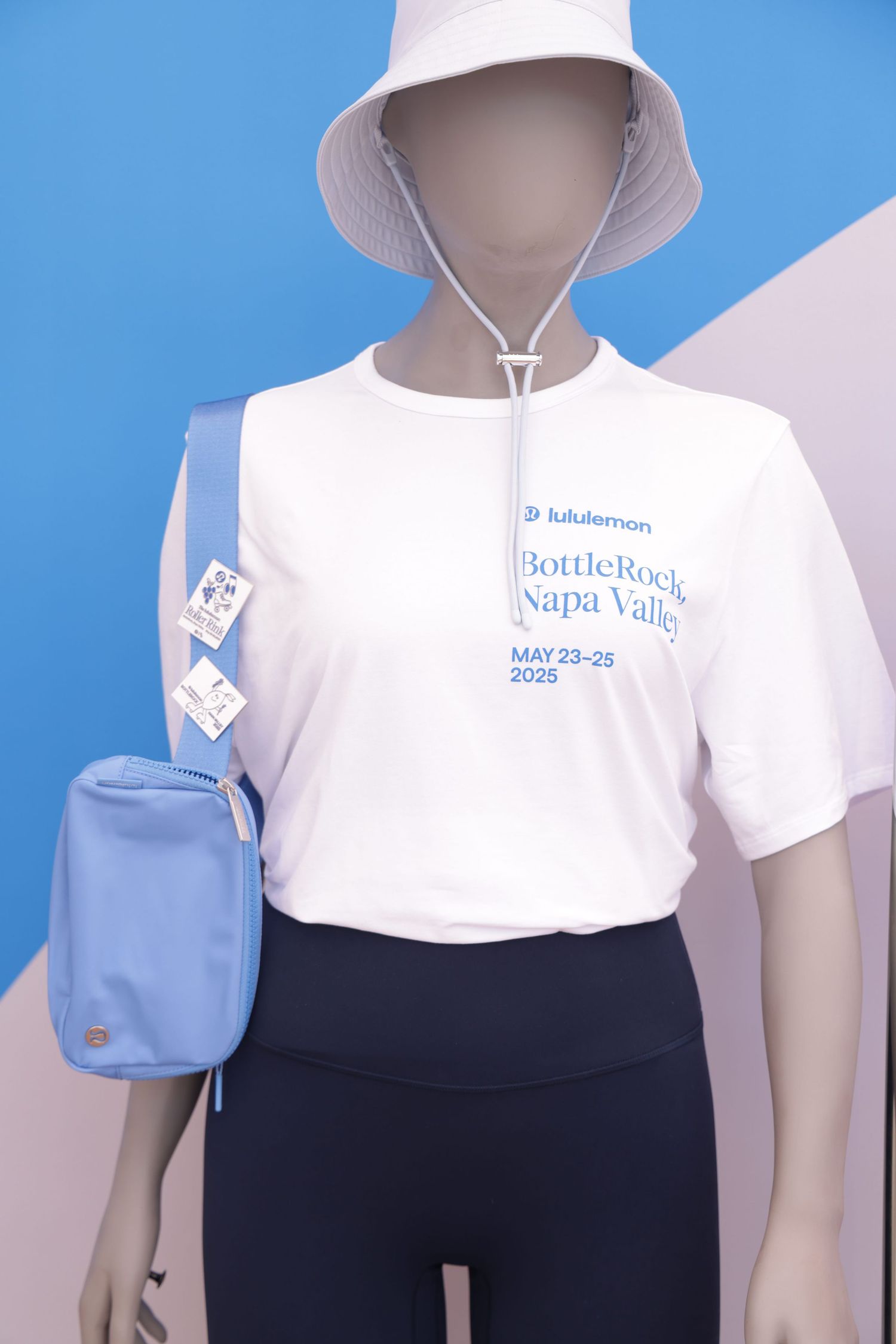 Retail store mannequin display wearing white polo shirt and black pants with blue bag accessory against blue background.