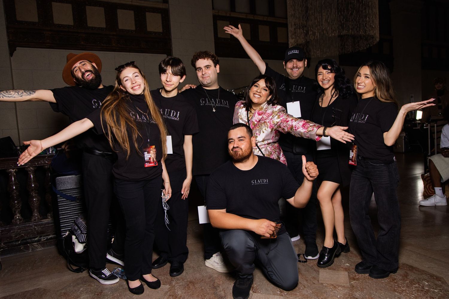 Group photo of fashion event staff members posing together in black outfits against stone wall backdrop.