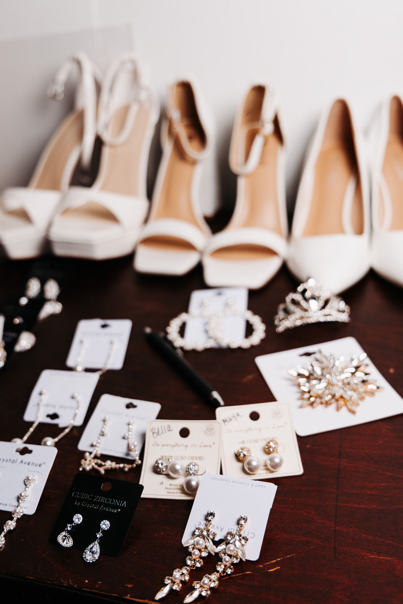 Wedding accessories including white heels and crystal earrings displayed on dark wooden surface.