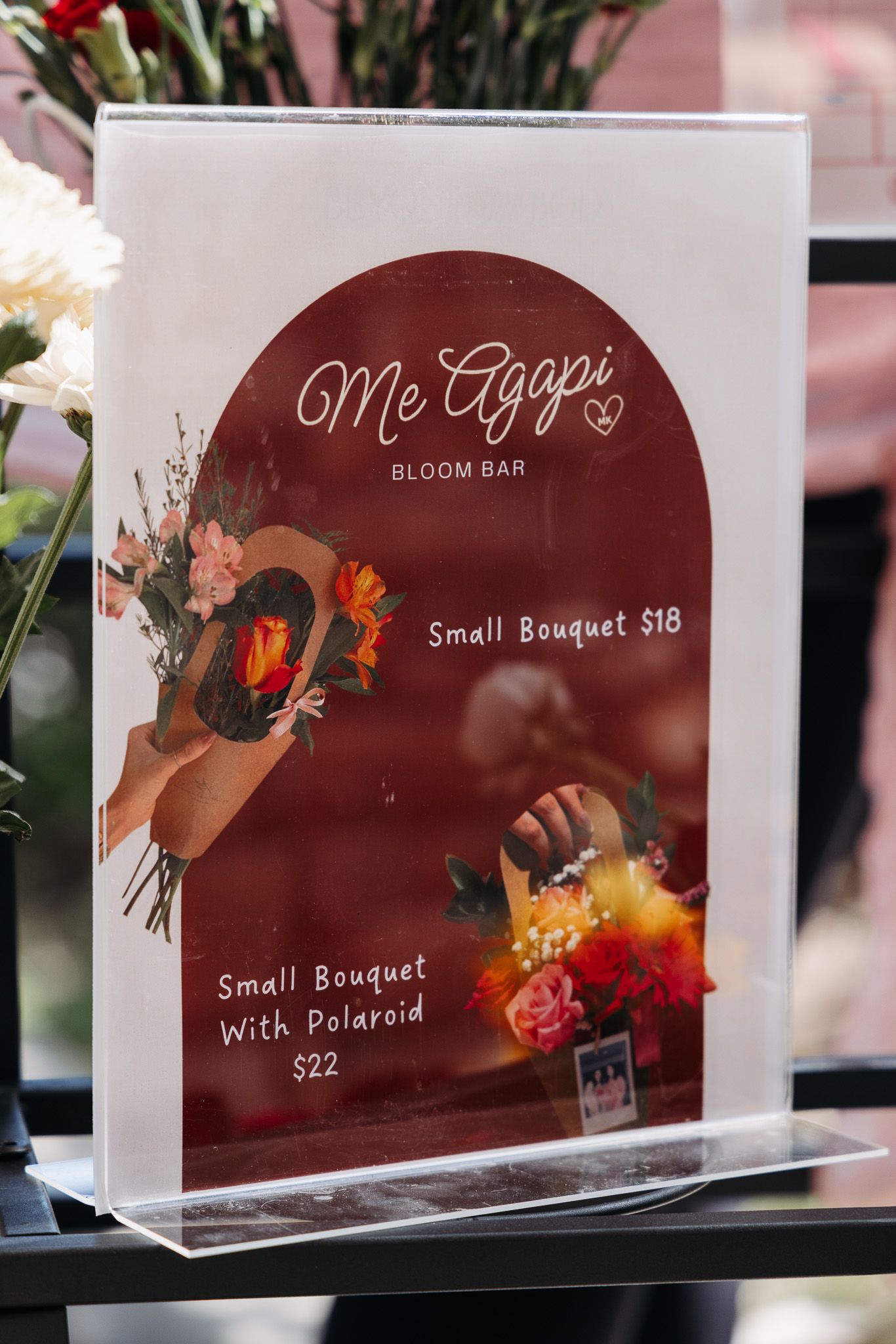 Menu display signs for Me Agapi flower shop showing bouquet prices and Polaroid options.