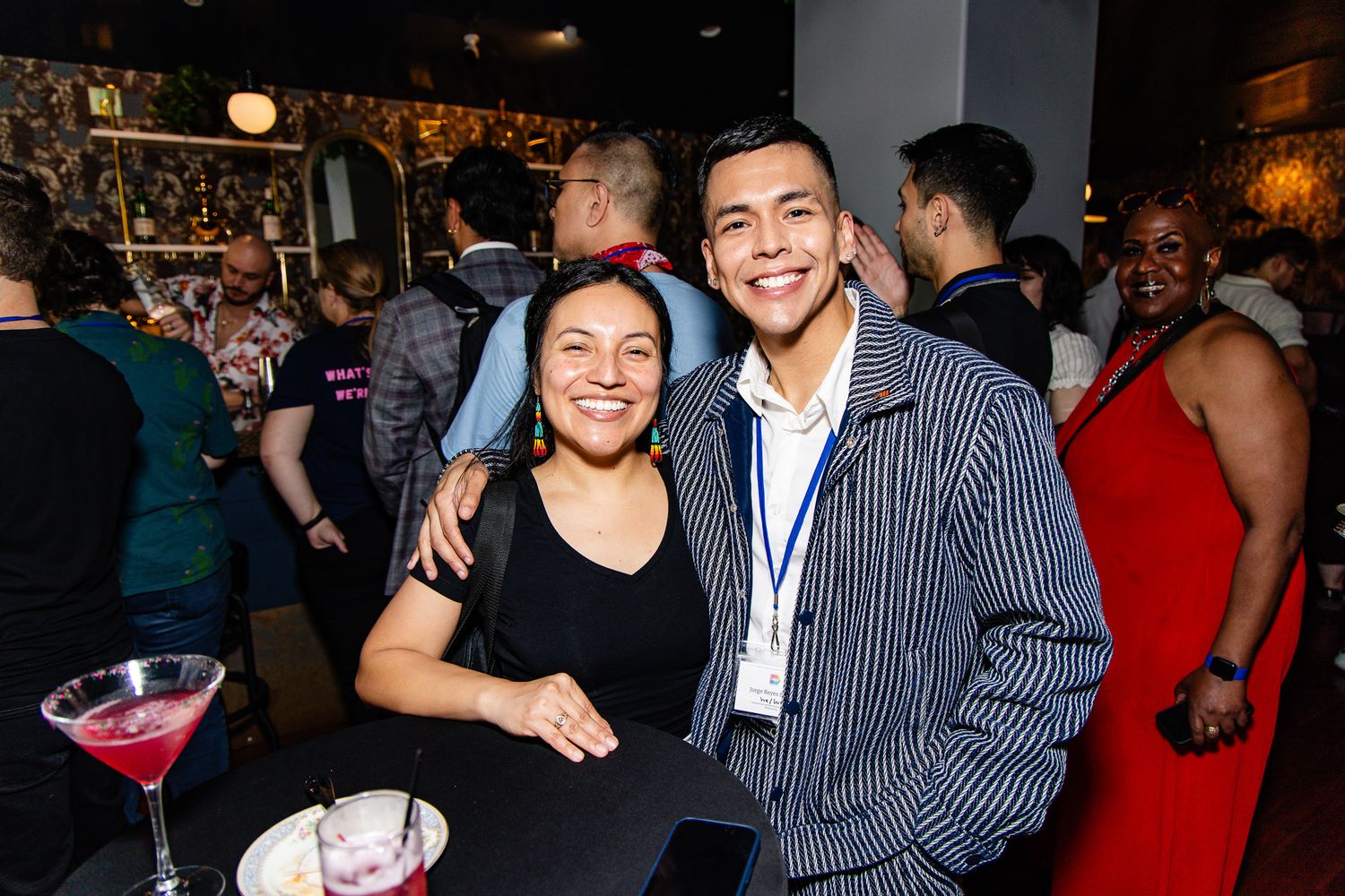Two people enjoying drinks and smiling together at a social gathering in a dimly lit bar setting.