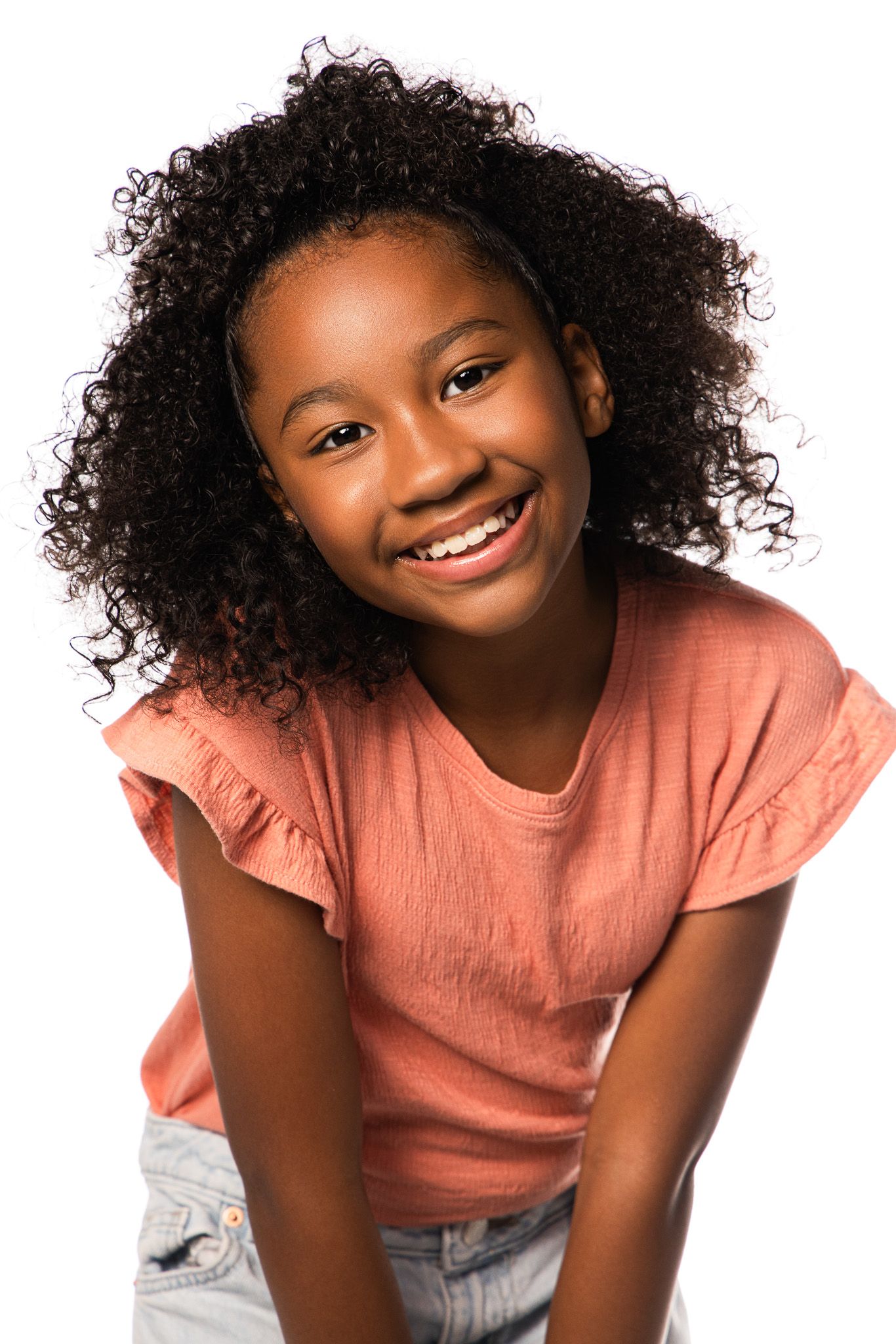 Studio portrait of a smiling youth in a coral t-shirt with natural curly hair.