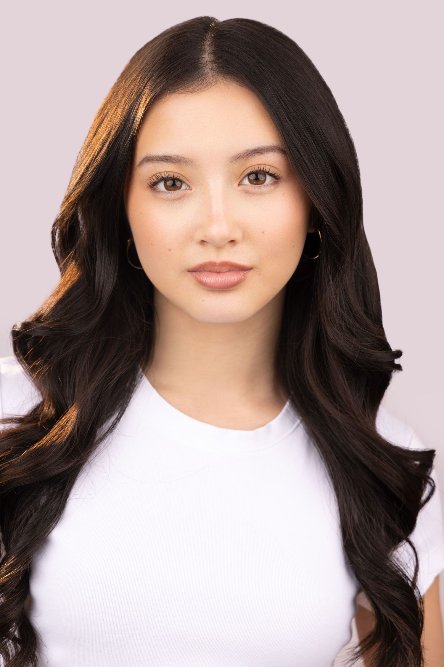 Elegant portrait with flowing dark waves and white top against soft pink background.
