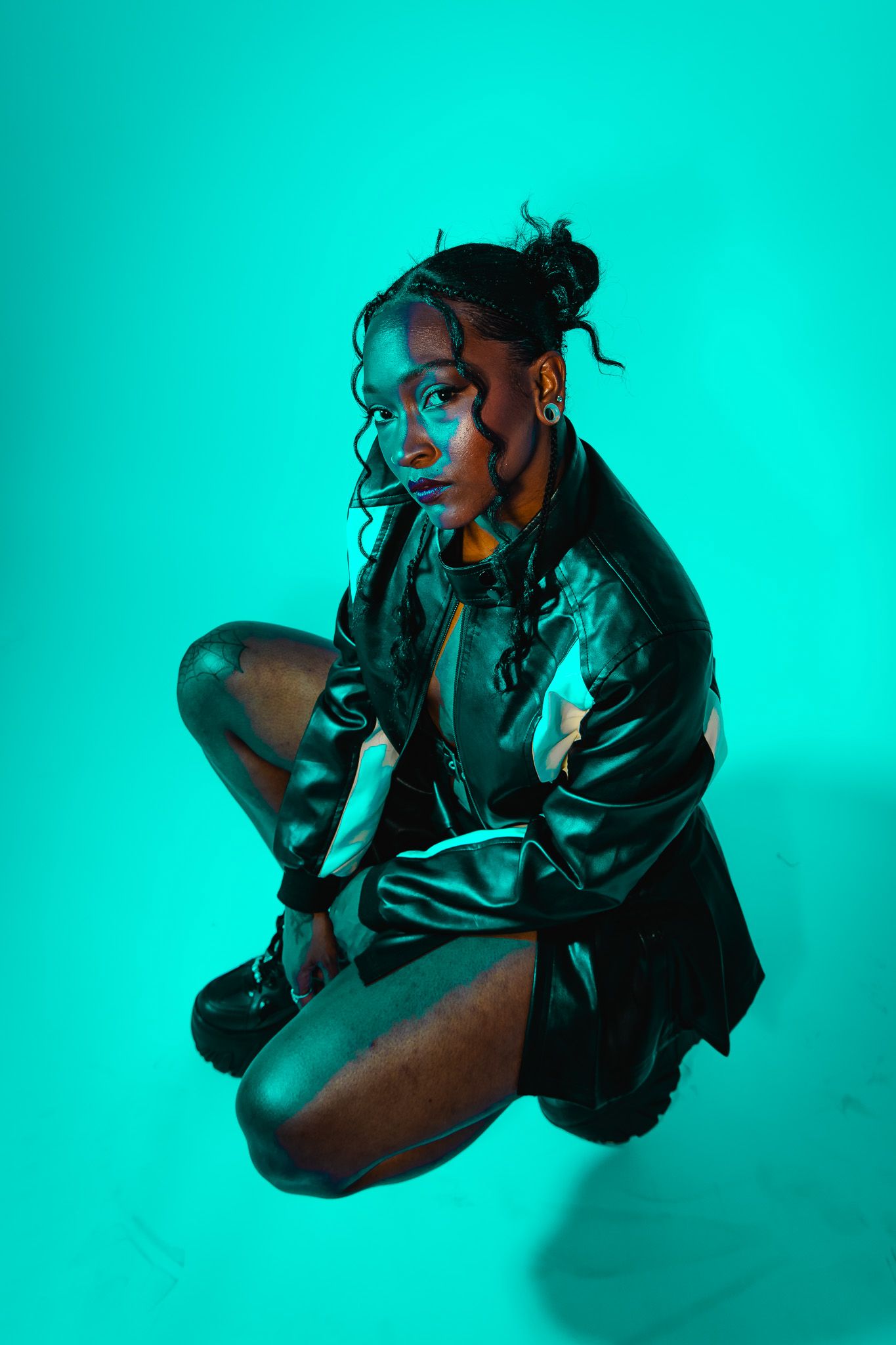 A figure in silhouette poses dramatically against a vibrant turquoise background with moody lighting.