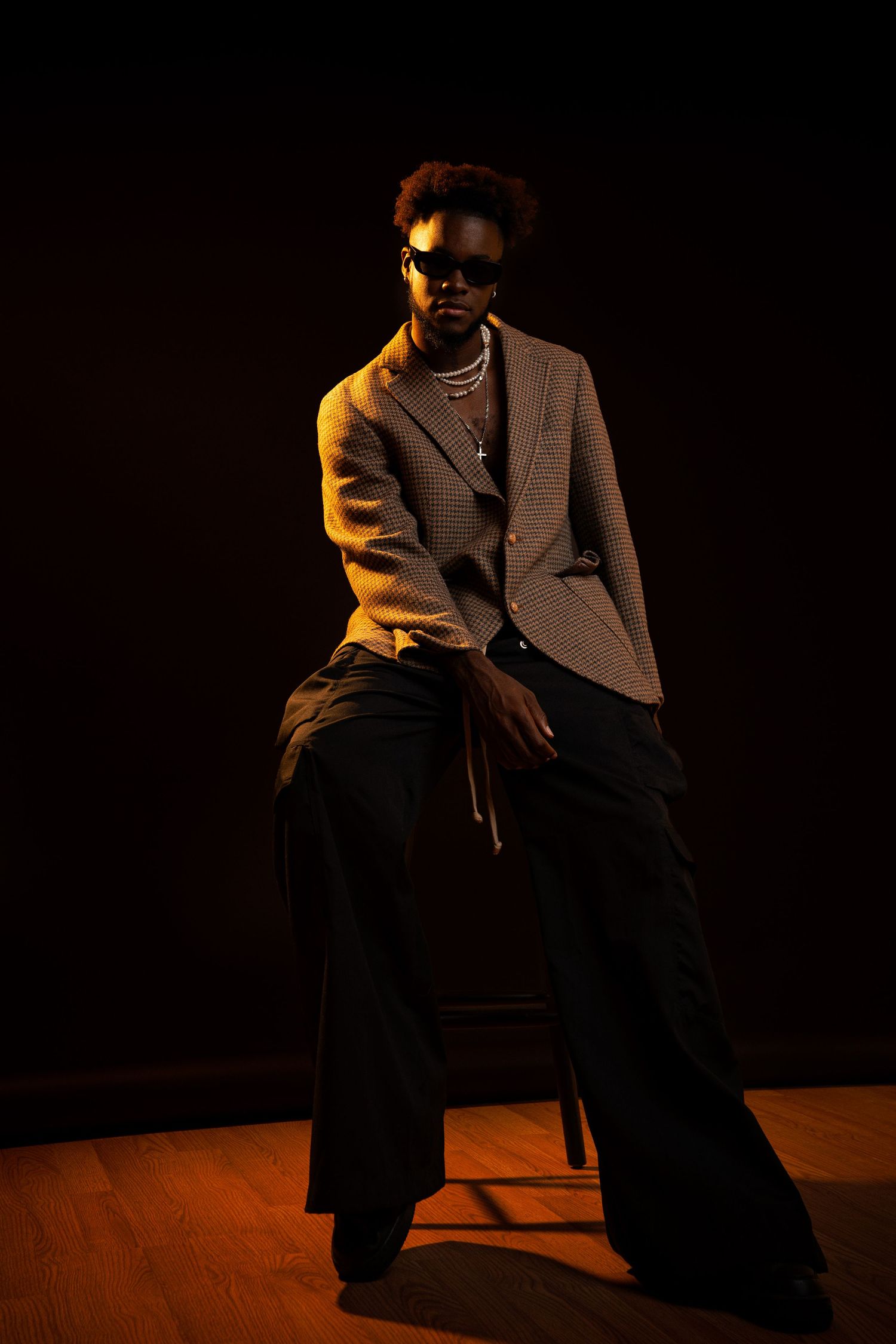 Artistic dark portrait series showing seated figure in brown coat against dramatic shadowy background with warm lighting.