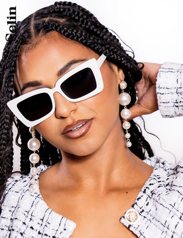 Stylish portrait featuring retro white sunglasses, pearl earrings, and textured black hairstyle against white background.
