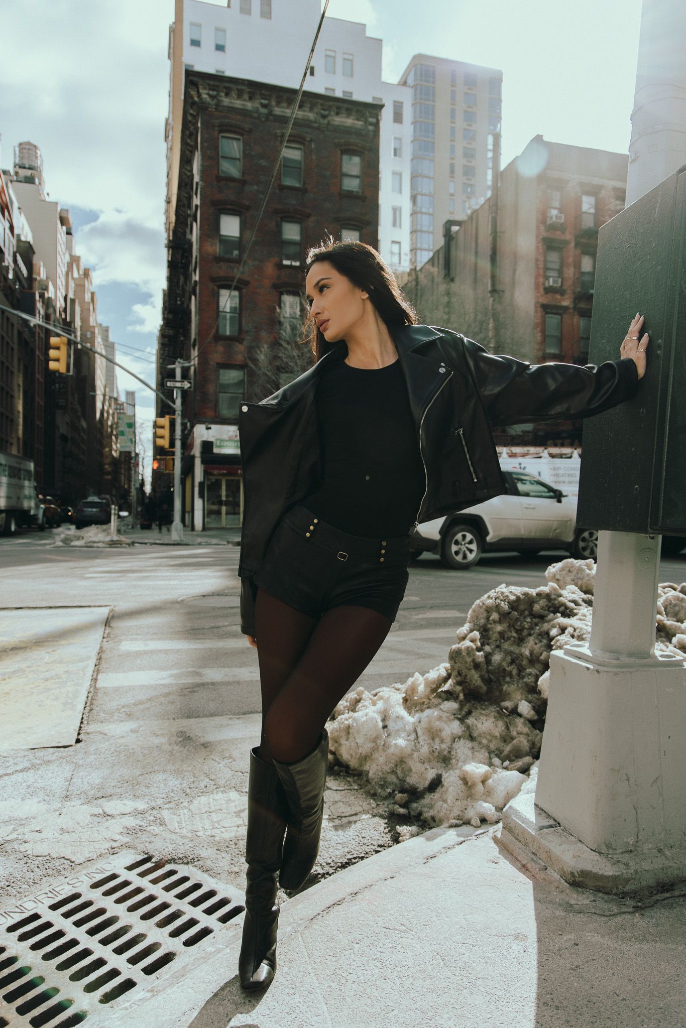 Stylish street fashion photo of someone posing against a column on a New York City sidewalk with snow piles nearby.