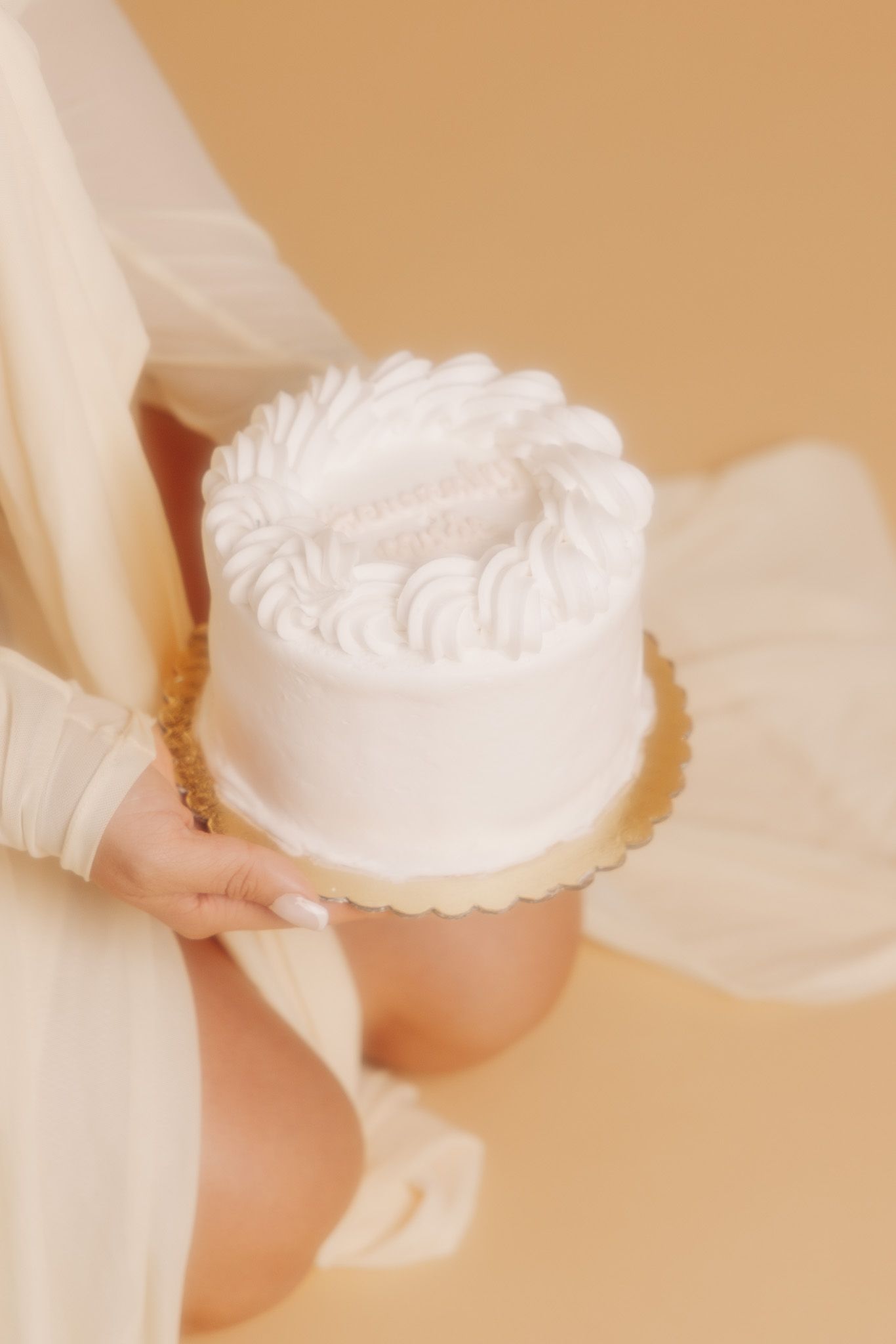 A white frosted cake with delicate piping details being displayed against a soft beige background with flowing fabric.